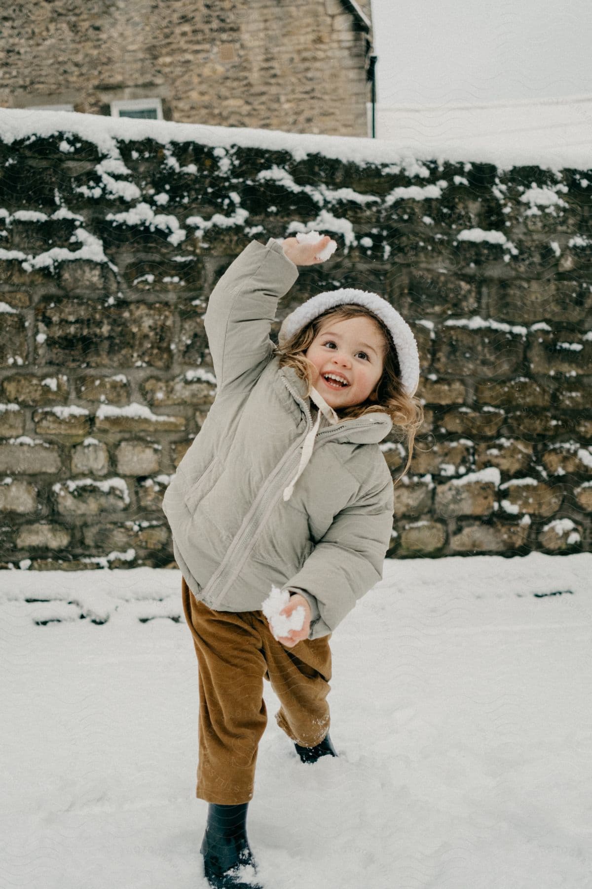 A little girl smiling while holding a snowball in a snowy environment