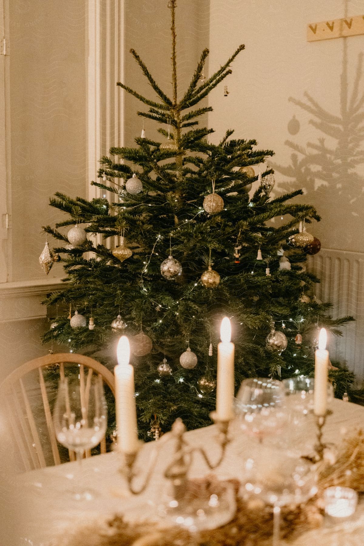 A small green Christmas tree with decorations in the corner of a wall.