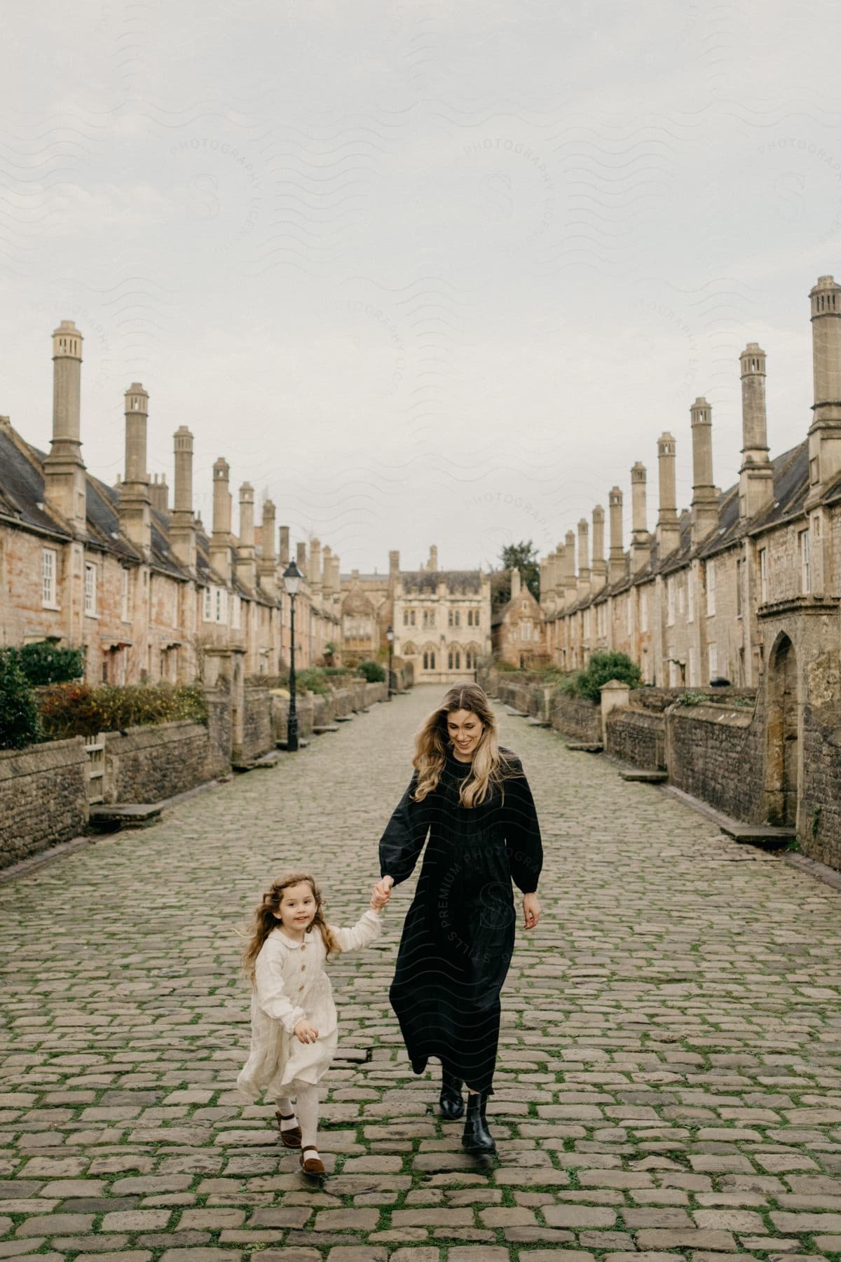 A mother and daughter are smiling and laughing as they hold hands walking down the brick walkway.