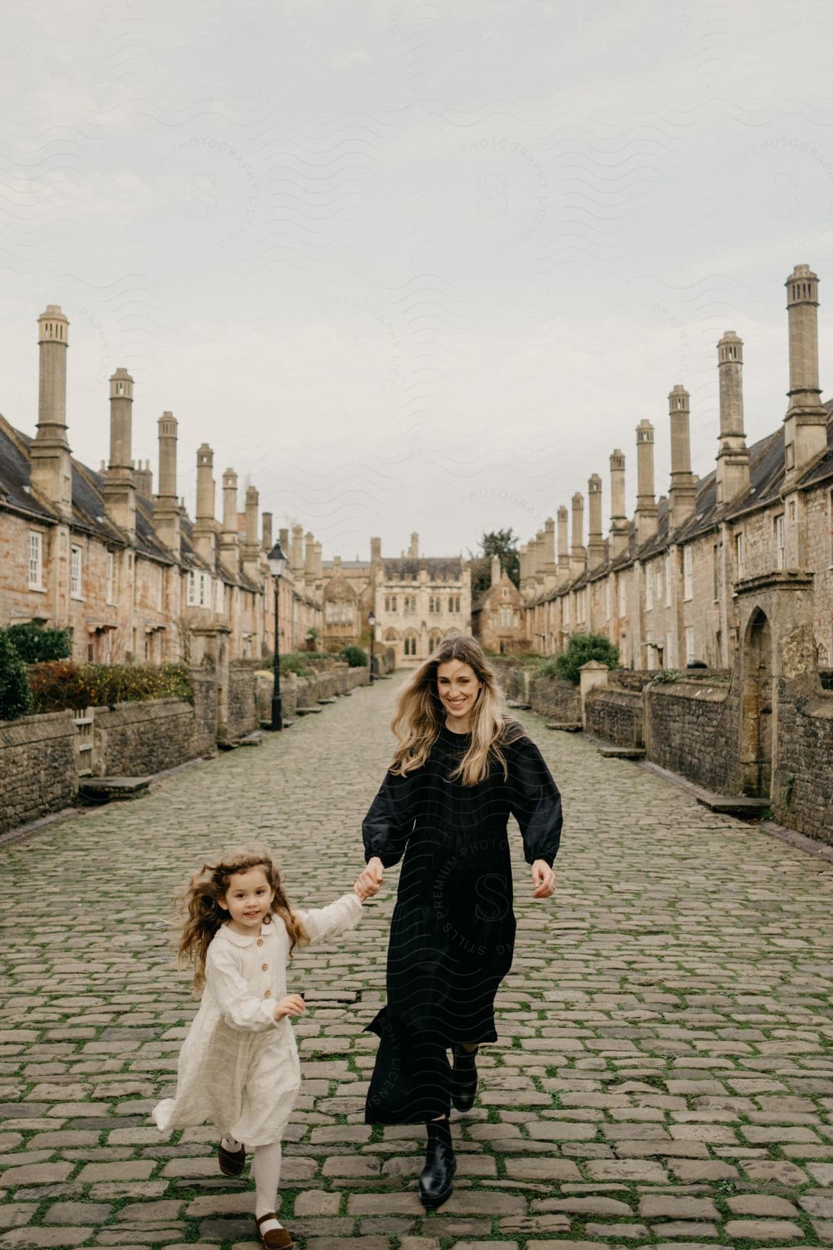 A mother and daughter walking on a stone path alongside several old residences.