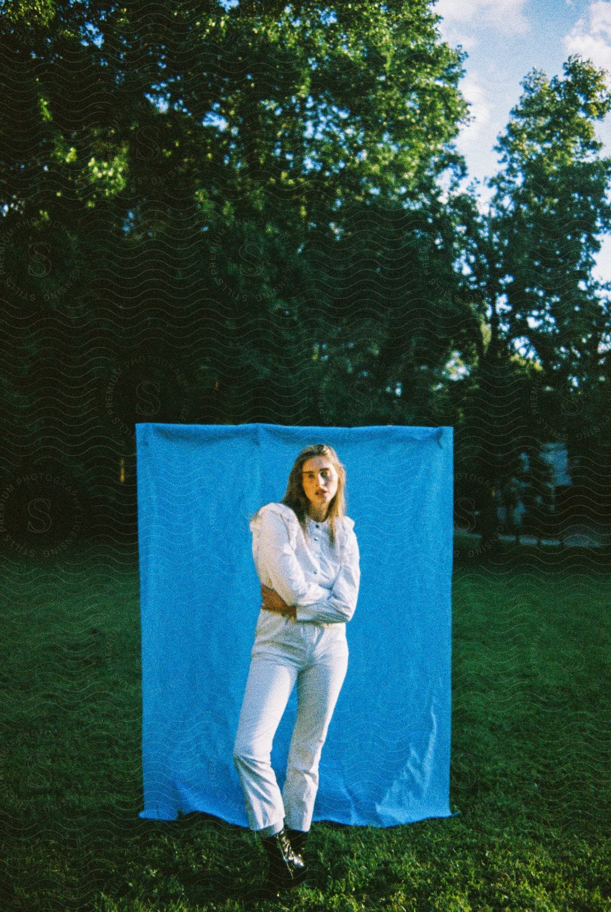 A women is standing in front of a blue blanket that is hanging up outside.
