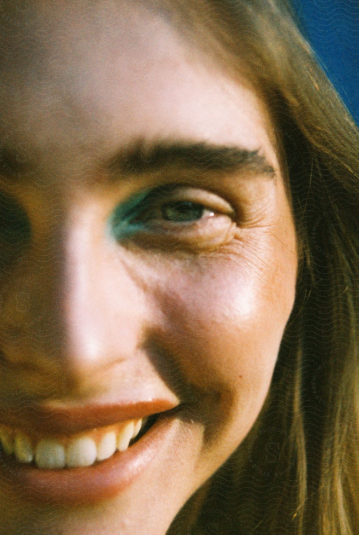 Half a woman's face is shown with blue makeup by her eye.