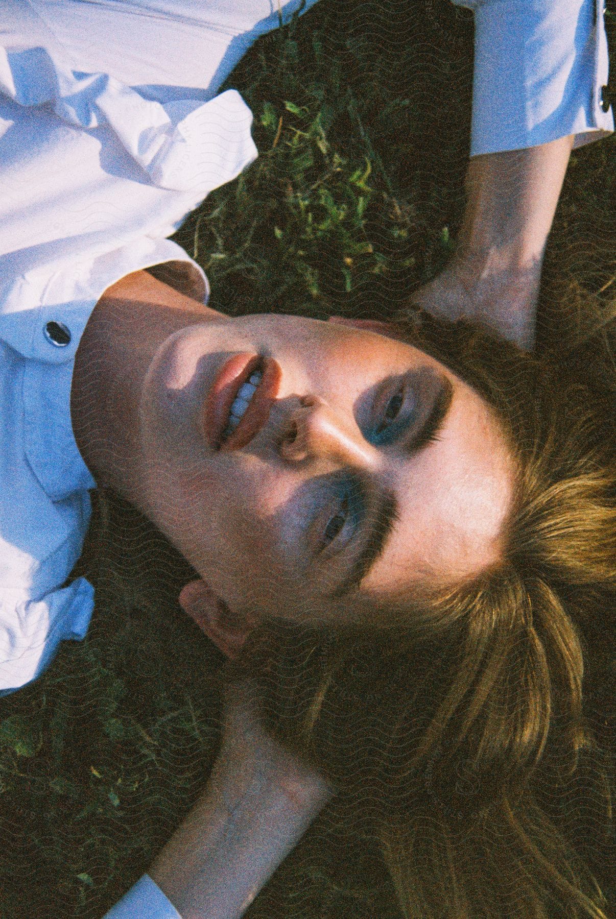 A man with brown hair, dressed in a white shirt, reclines on a green lawn