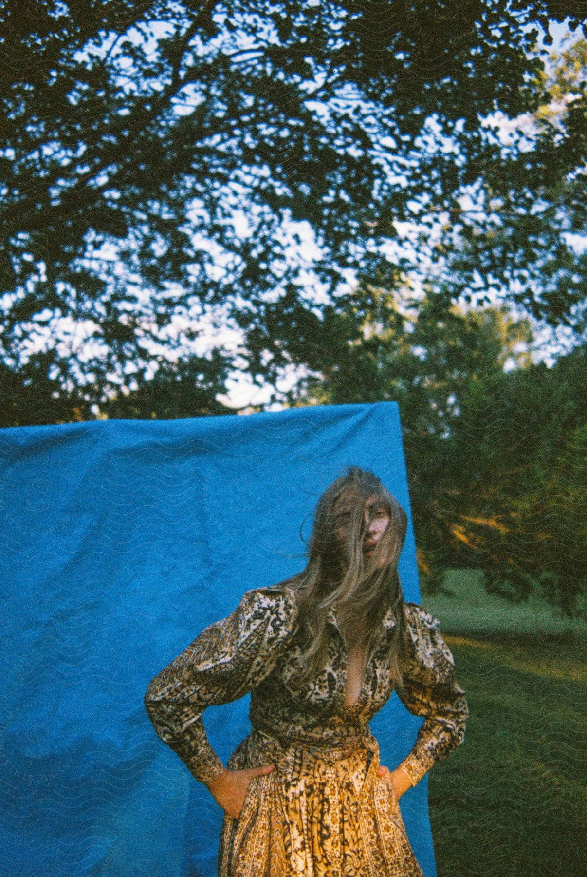 A Women Is Standing In Front Of A Hanging Blue Blanket On A Windy Day