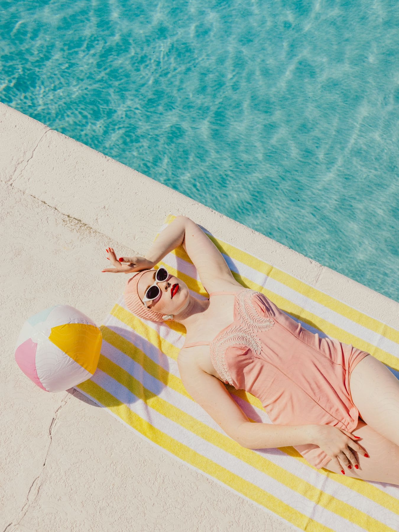 A woman in a swimsuit is sunbathing next to a pool with crystal clear water.