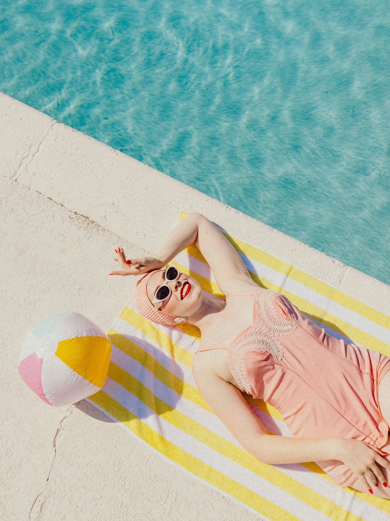 Woman lying on a towel sunbathing next to a pool.