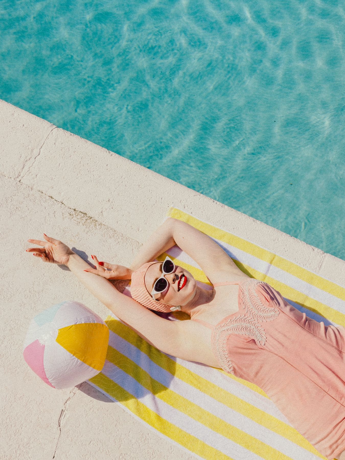 A woman modeling a vintage swimsuit while laying next to a pool.