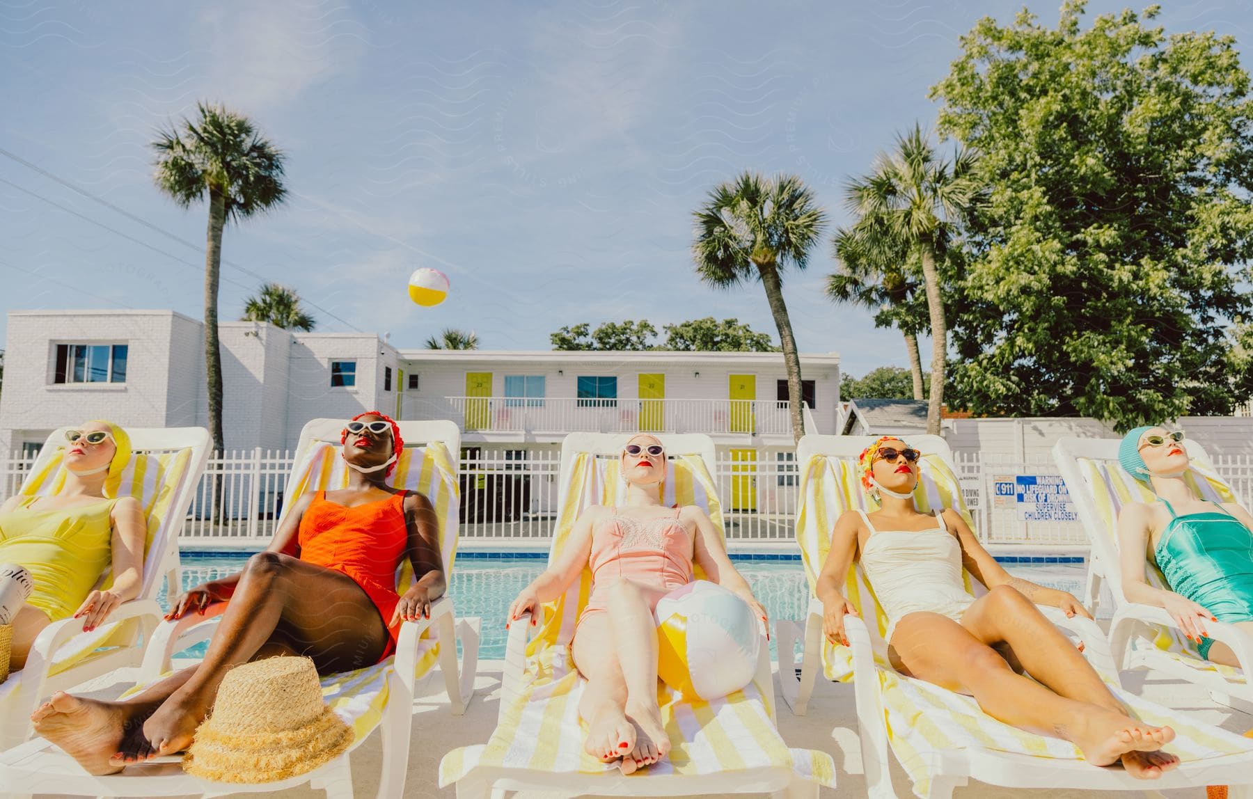 Five women in colorful wetsuits are lying down in the sun behind a pool.