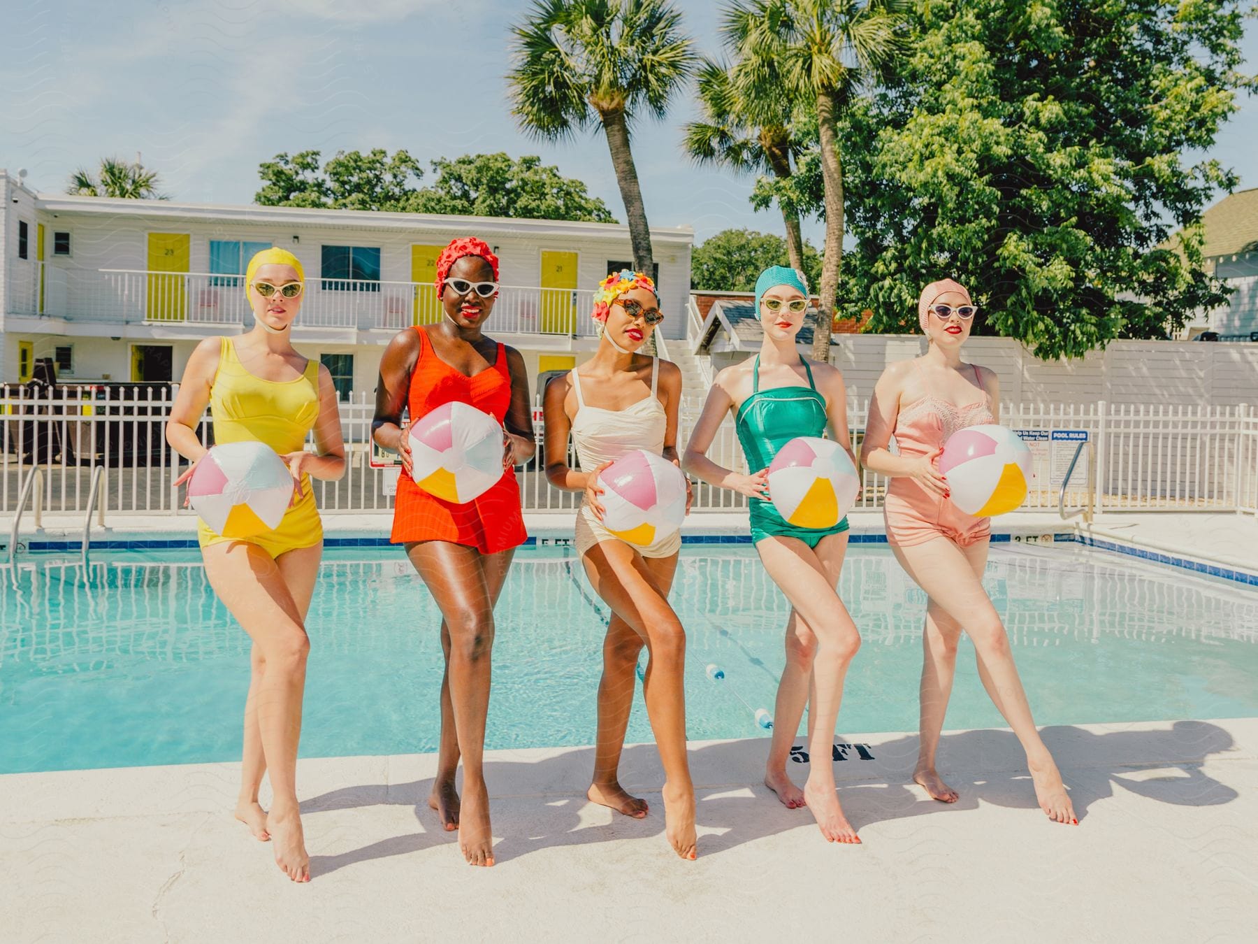 Young women in swimsuits, standing by the pool with their backs to the camera, holding a ball.