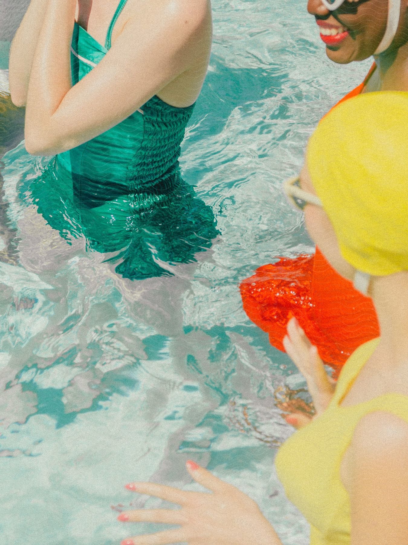 Three women out in a pool modeling some vintage swimsuits.