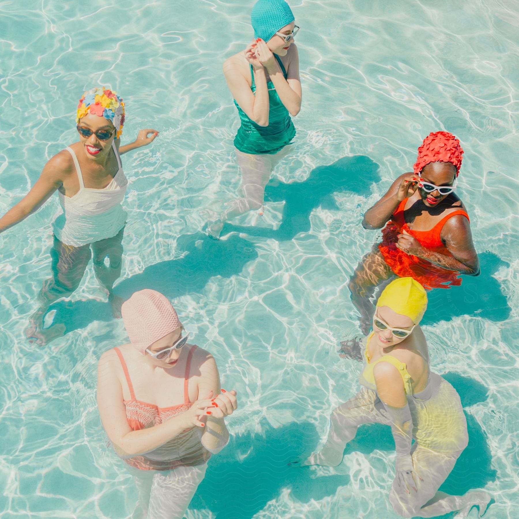 Five women in colorful swimwear in a pool with crystal clear water.