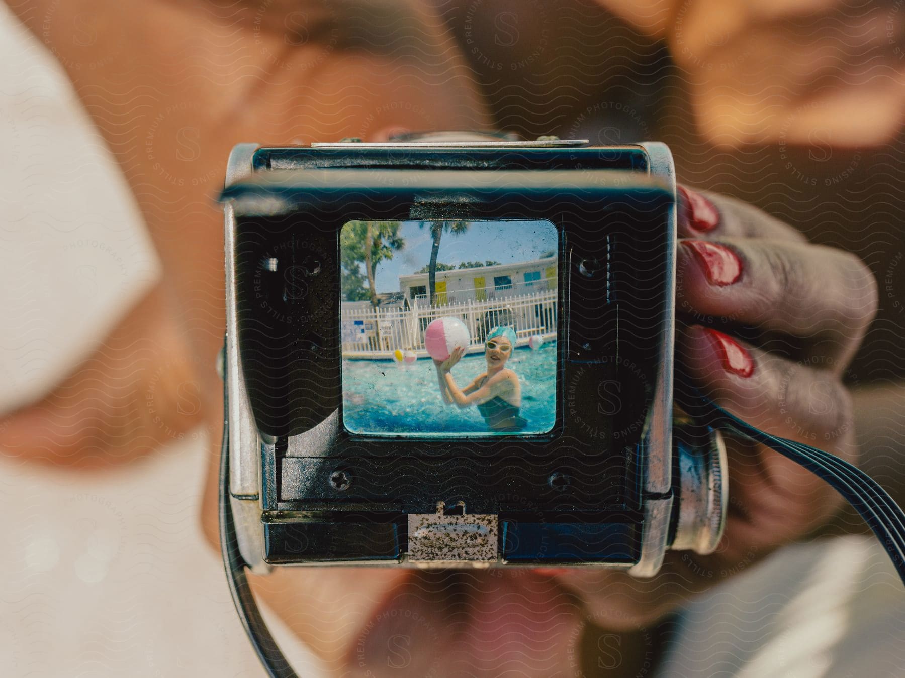 Stock photo of close-up of a woman holding a camera that displays another woman in a swimsuit, holding a beach ball in a swimming pool