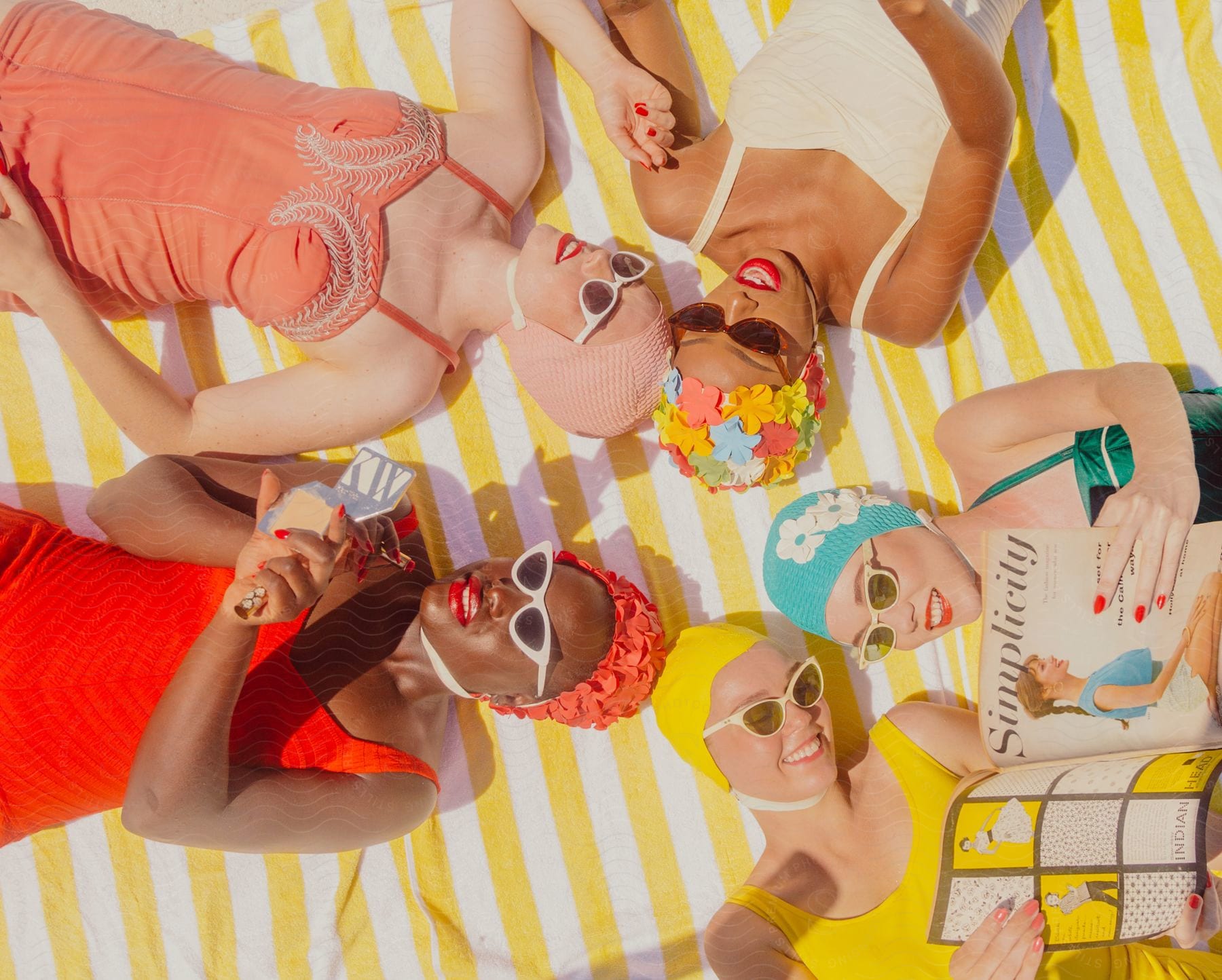 Five women in colorful swimming costumes are lying in circular shapes and smiling.