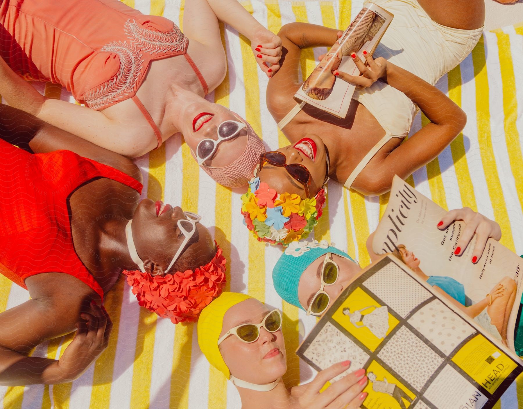 Five women in colorful swimming costumes are lying in circular shapes and smiling while reading magazines.