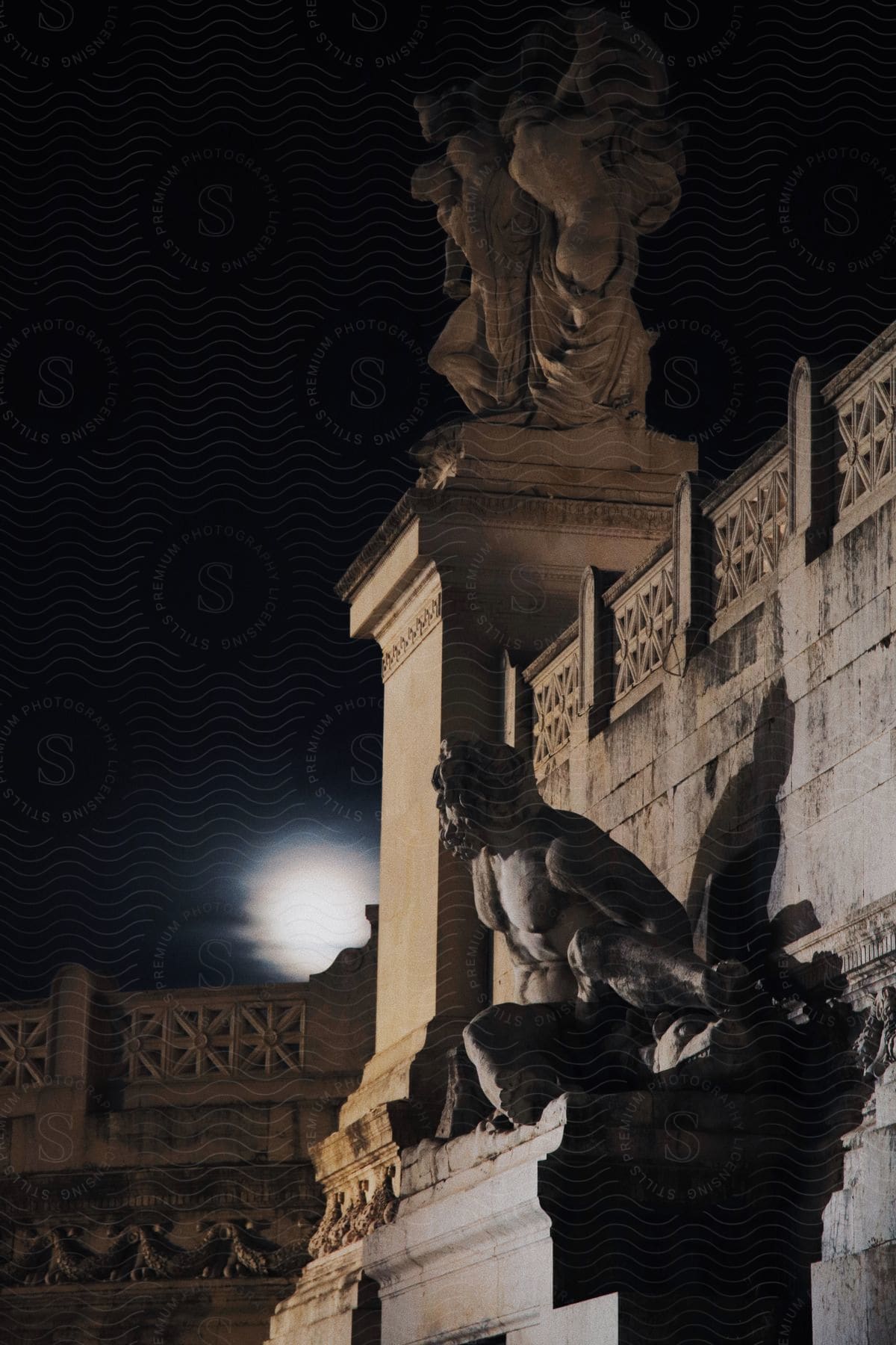 An ancient building stands with a statue in front and on top of a large square column