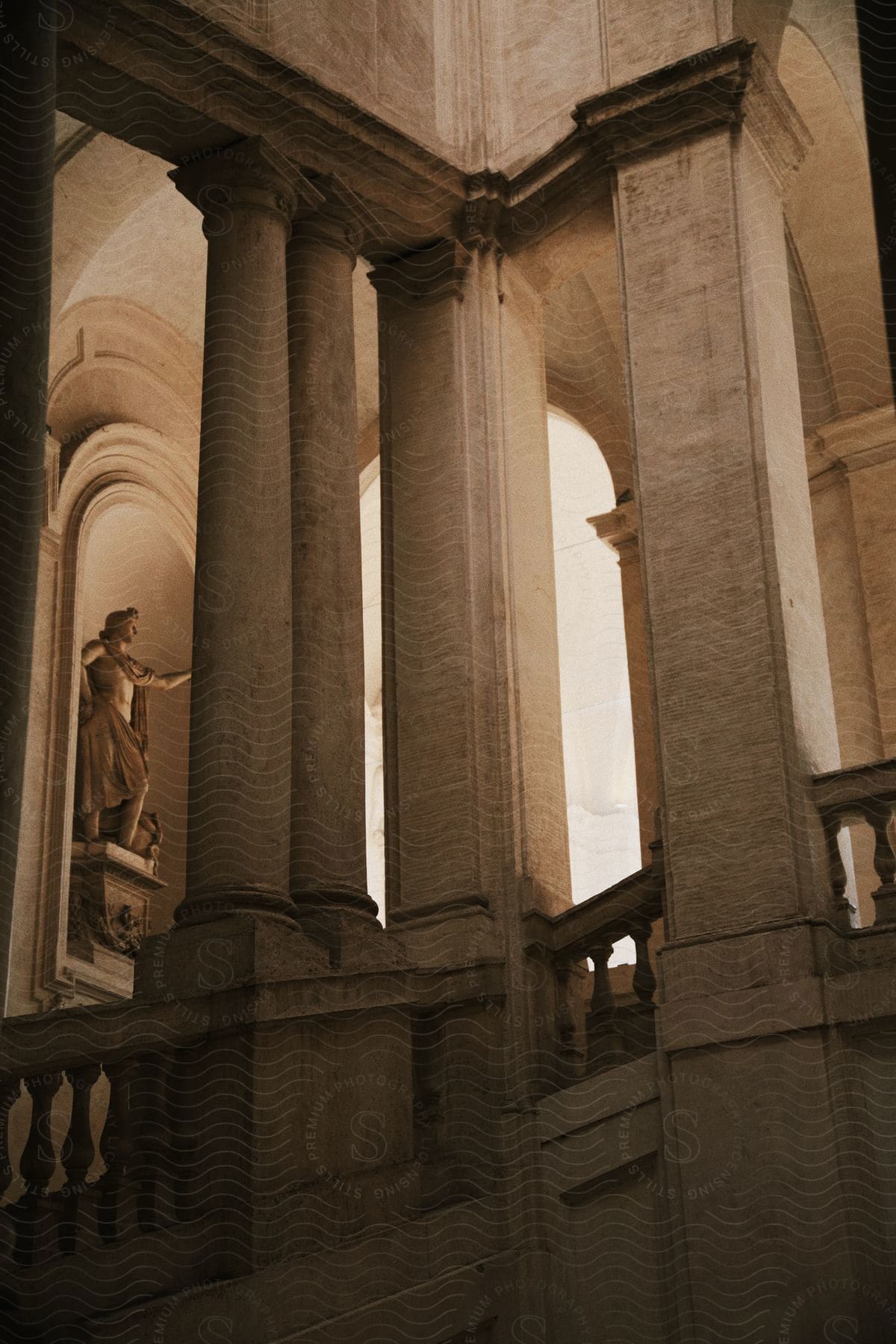 Columns surround stairs in an ancient building with a statue inside a wall arch