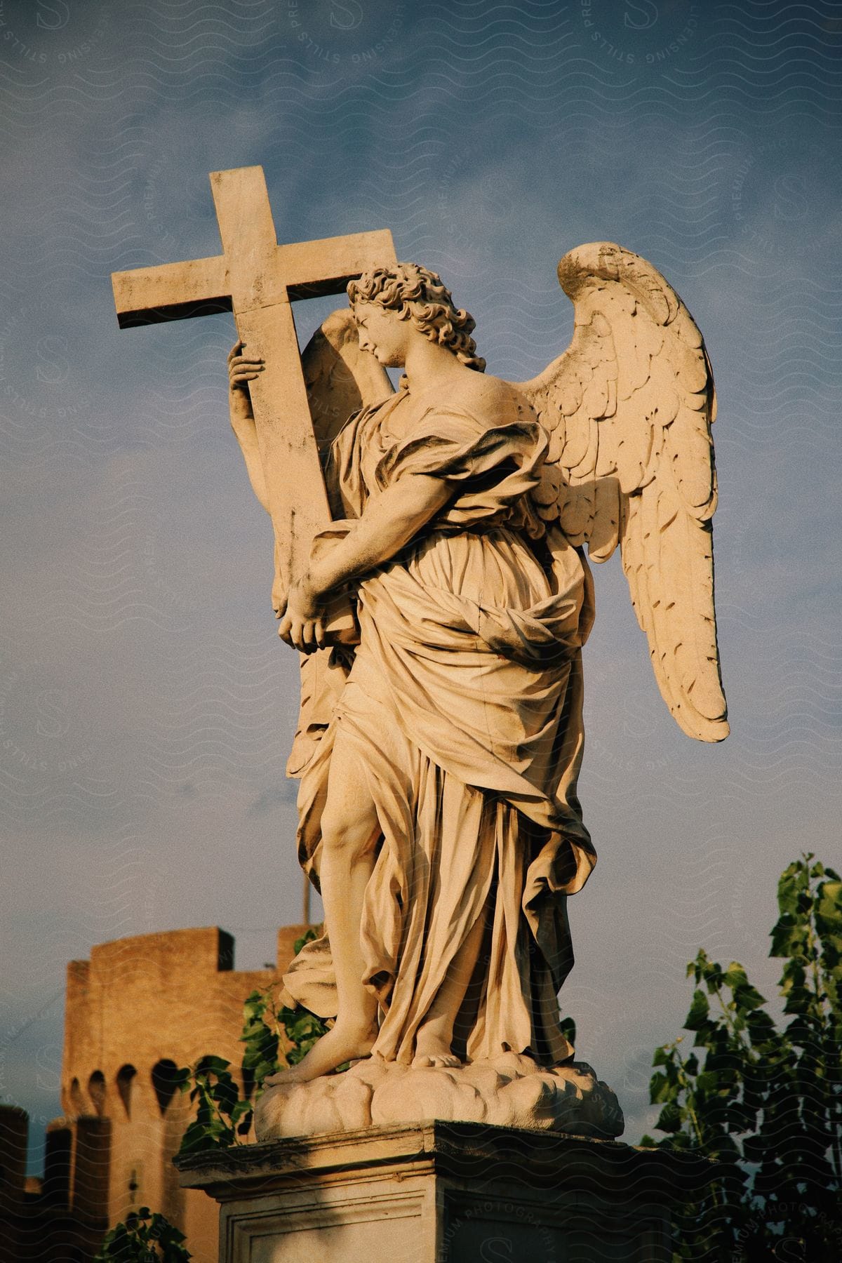 An outdoor statue of an angel holding a large cross under mostly cloudy skies.