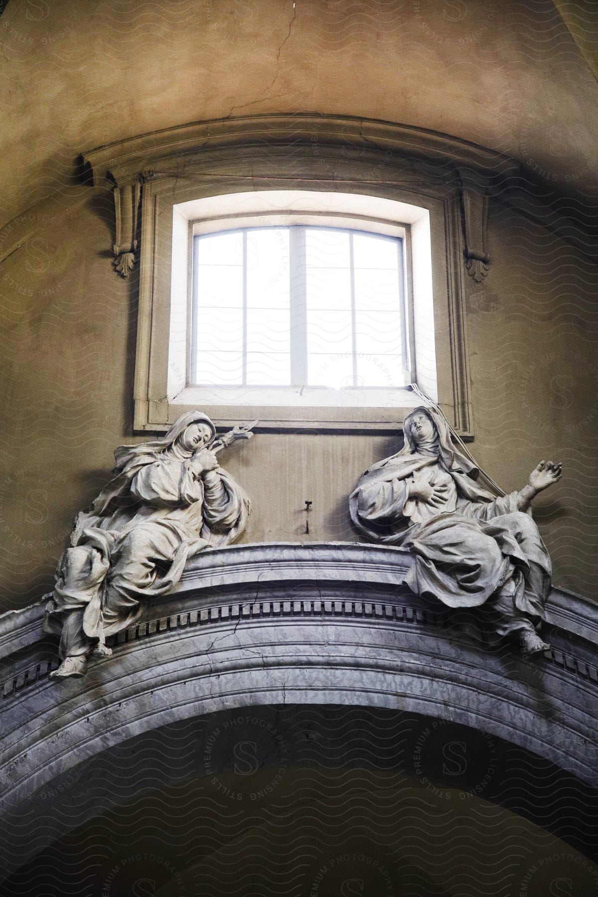 Two ancient statues of women on top of a passage and above there is a window.