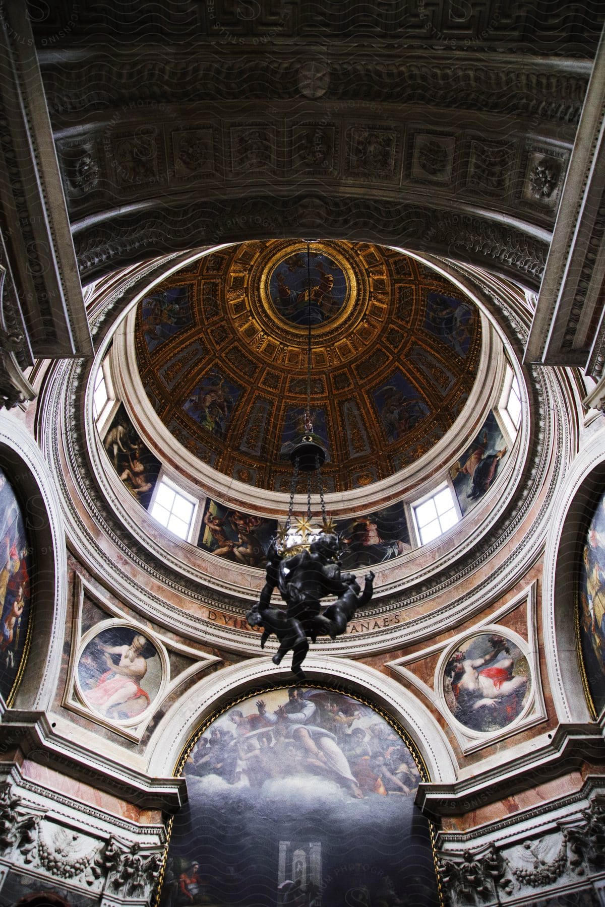 A round old architectural ceiling with various decorations and statues hanging.