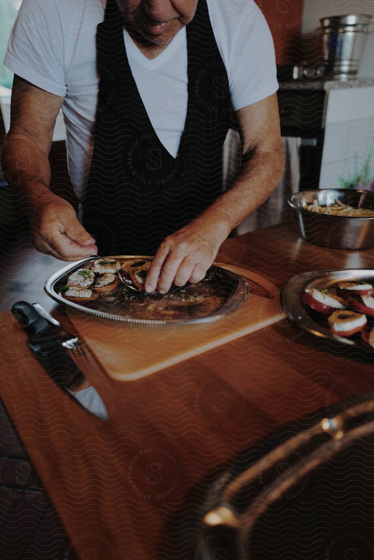 A man in a white shirt and a black apron takes food from a tray in the kitchen