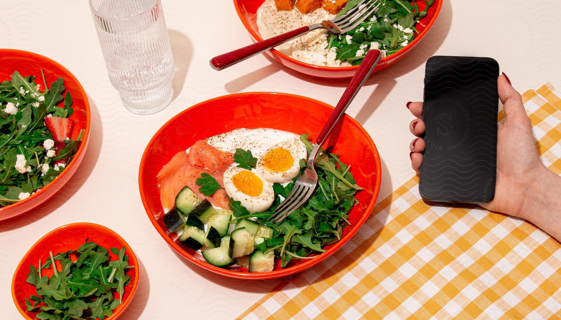 person holding a cell phone in front of a bowl of food with vegetables, including lettuce, tomatoes, cucumbers, and hard-boiled eggs.