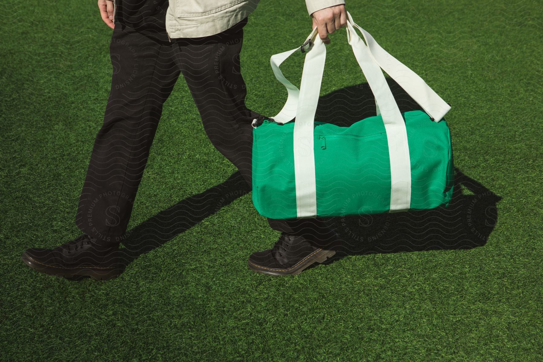 A man is carrying a green duffle bag as he walks across the grass