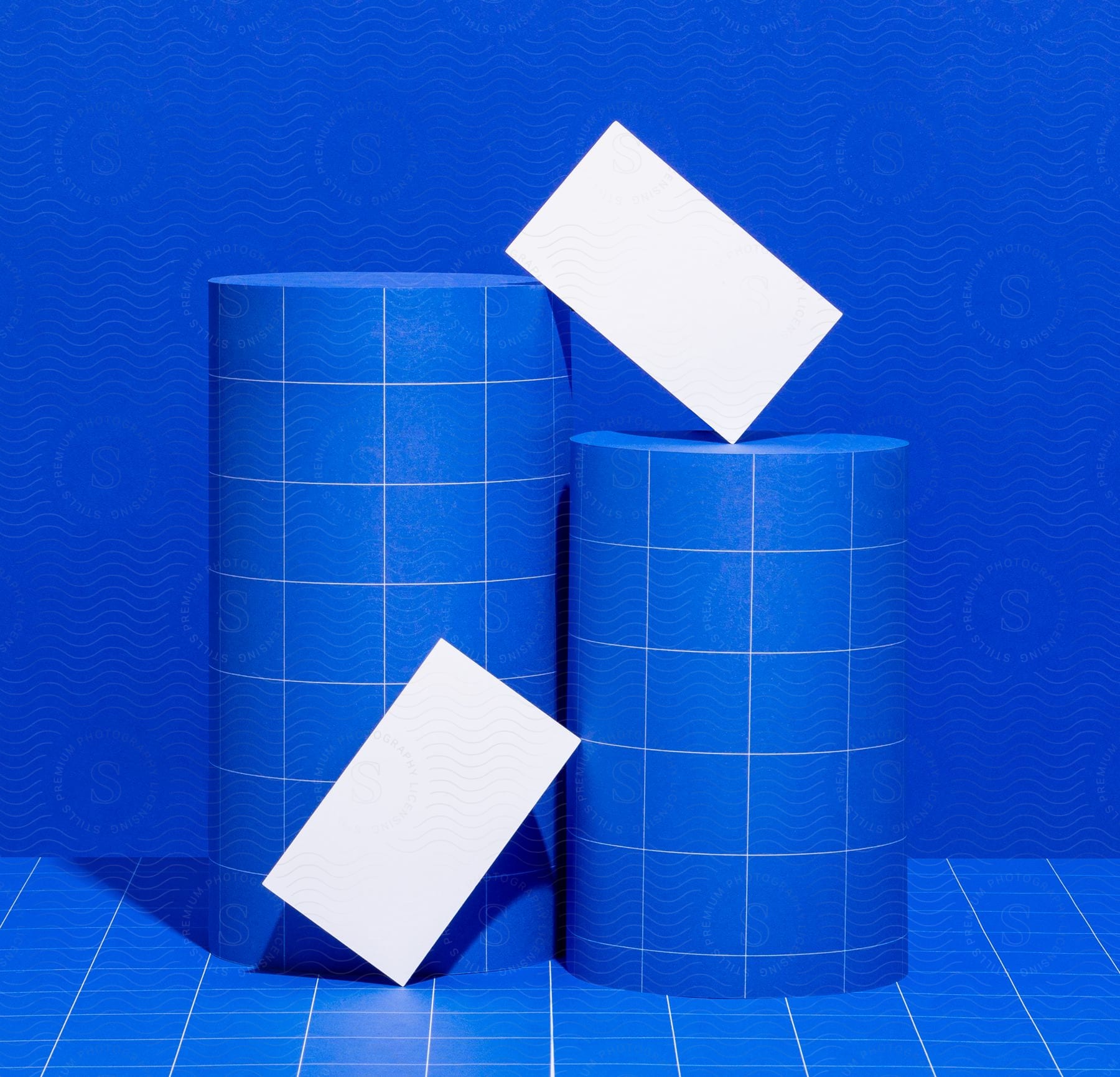 Two blue rolls with white squares on top, on a blue background with a white square, on a blue checkered table with white stripes.