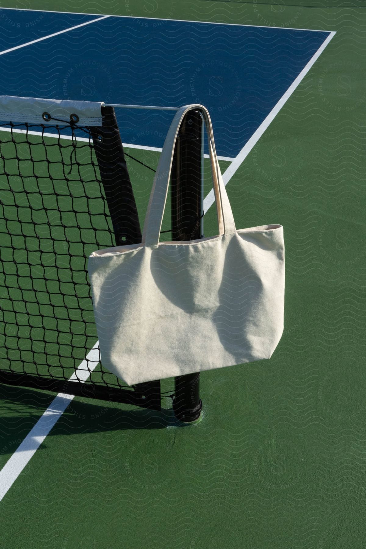A canvas tote bag hangs on a black post on a tennis court.