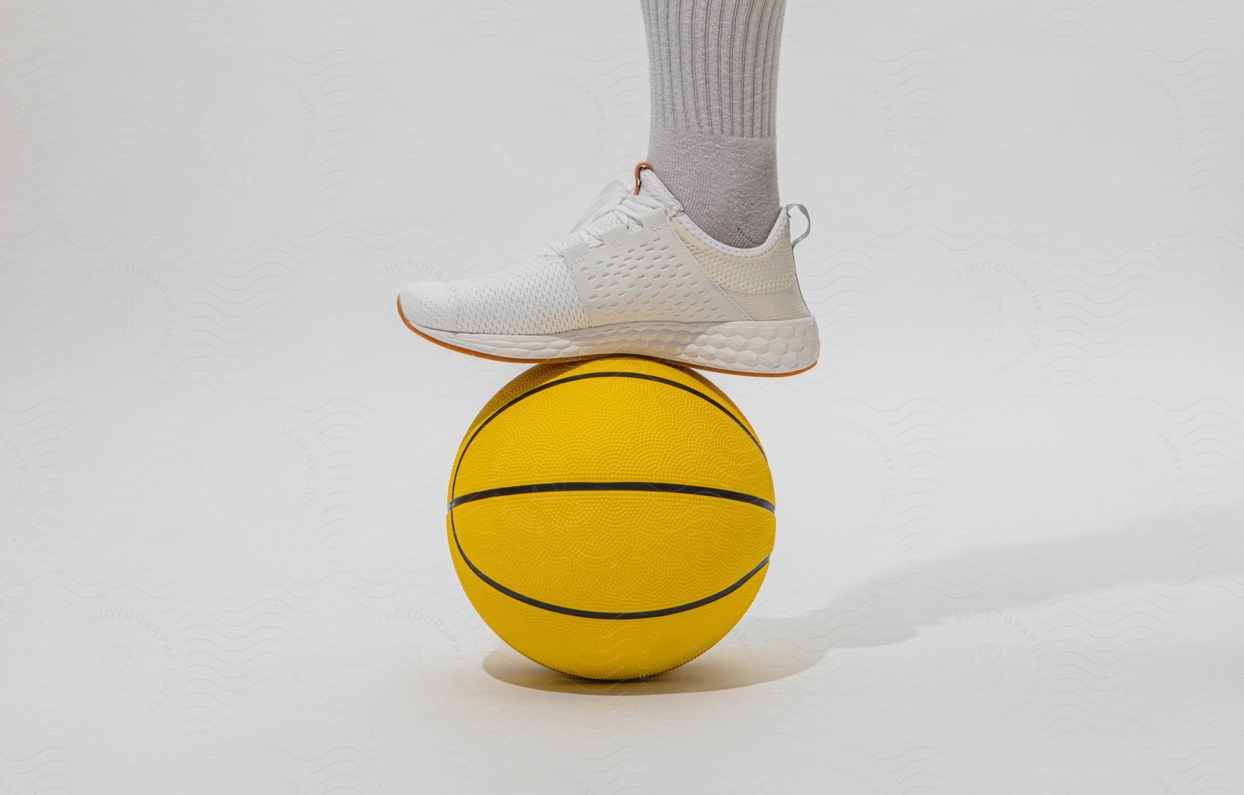 A Foot Wearing A White Sneaker And Gray Sock On Top Of A Yellow Basketball