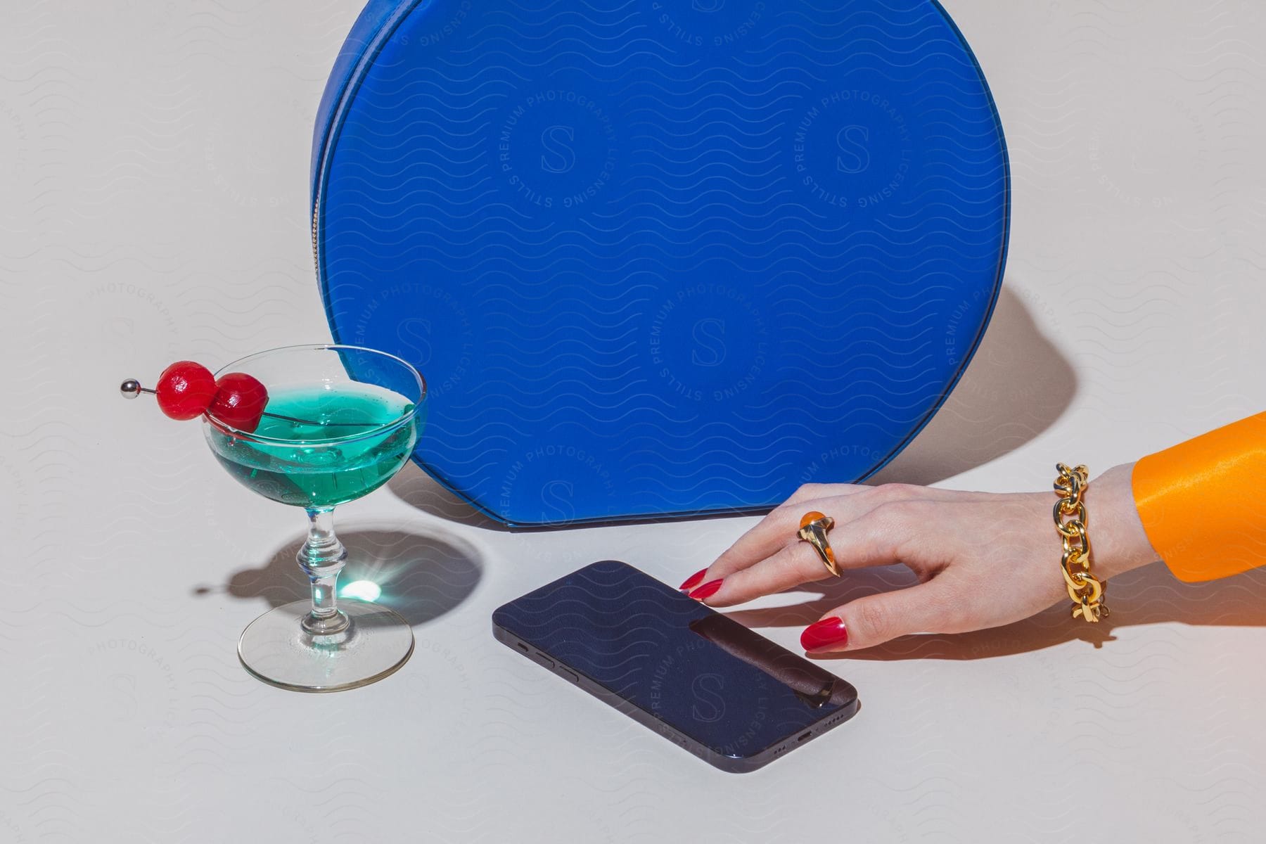 Stock photo of a woman is attempting to touch a smartphone with a cup of blue green drink  is sitting next to the phone.