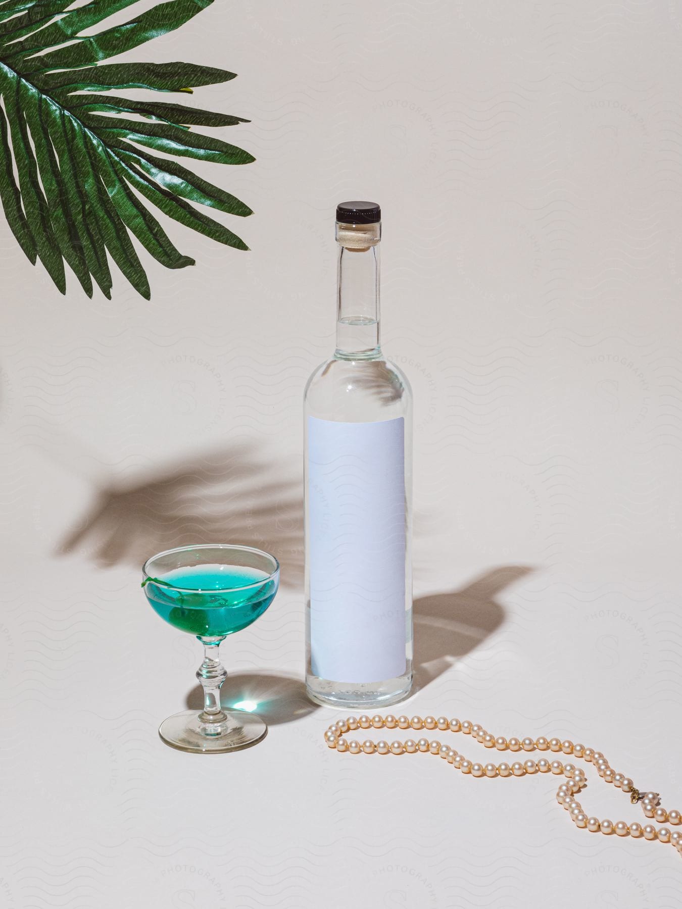 An empty wine bottle is paired with glassware that contains a blue green liquid.