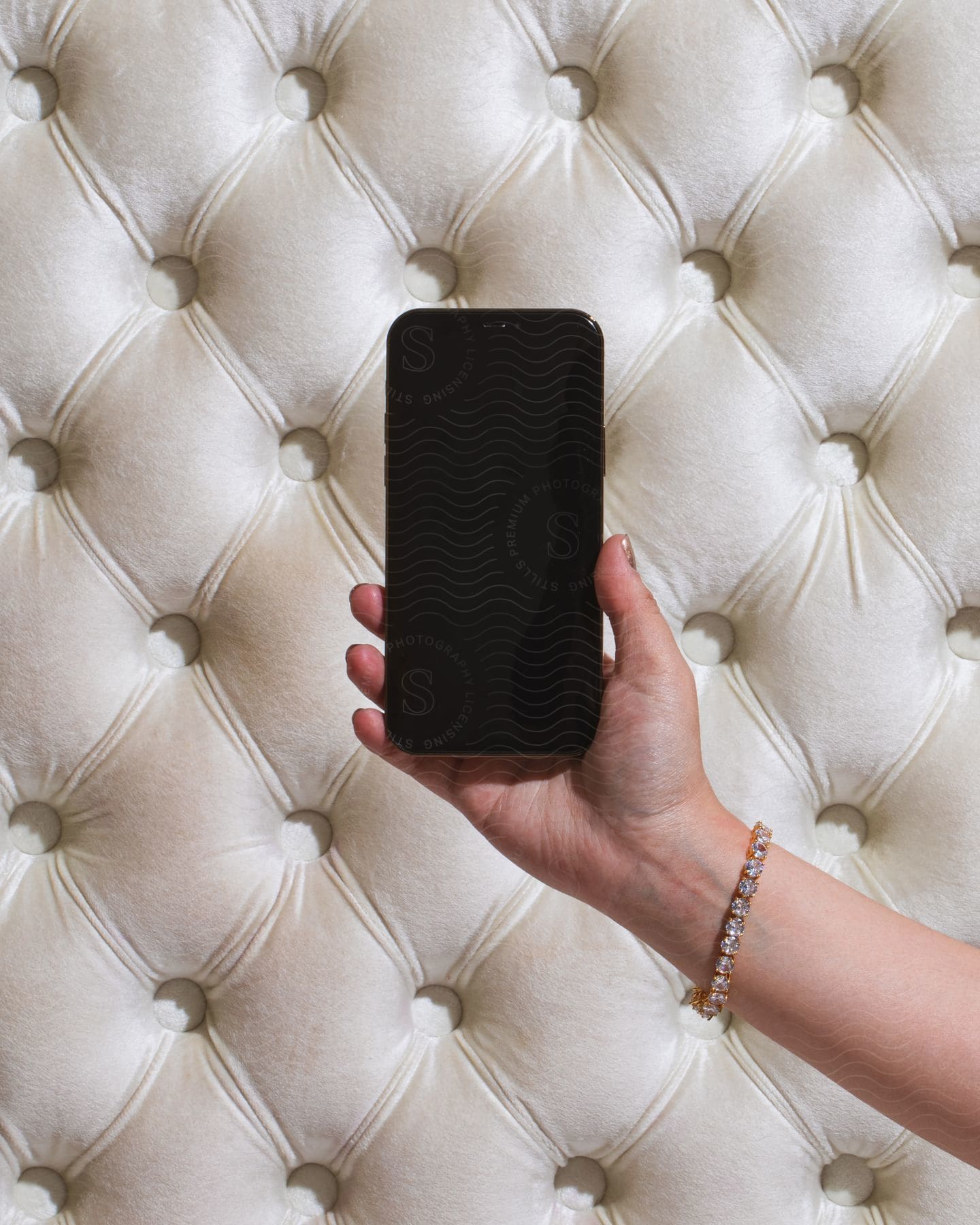 A person with a black cell phone and a diamond bracelet rests on a white diamond crease couch.