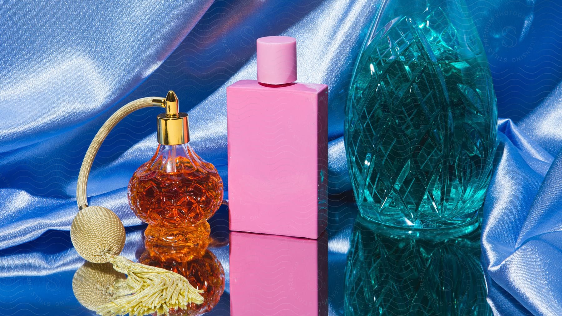 Three bottles of perfume are placed by each other on a mirror with a blue background.