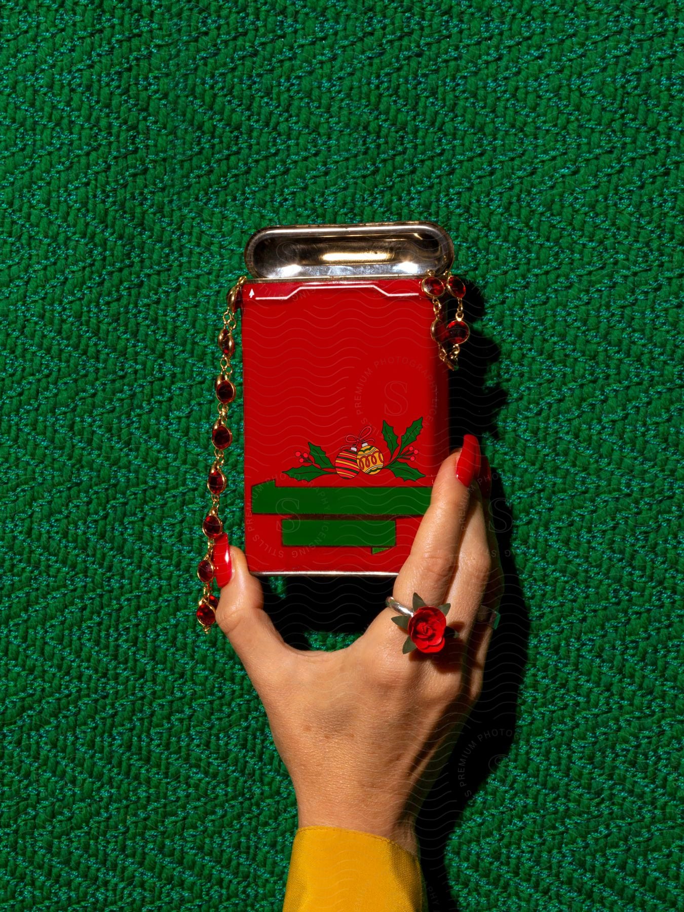 A woman with painted nails and a flower ring, holds a metal tin with jewelry hanging from it.