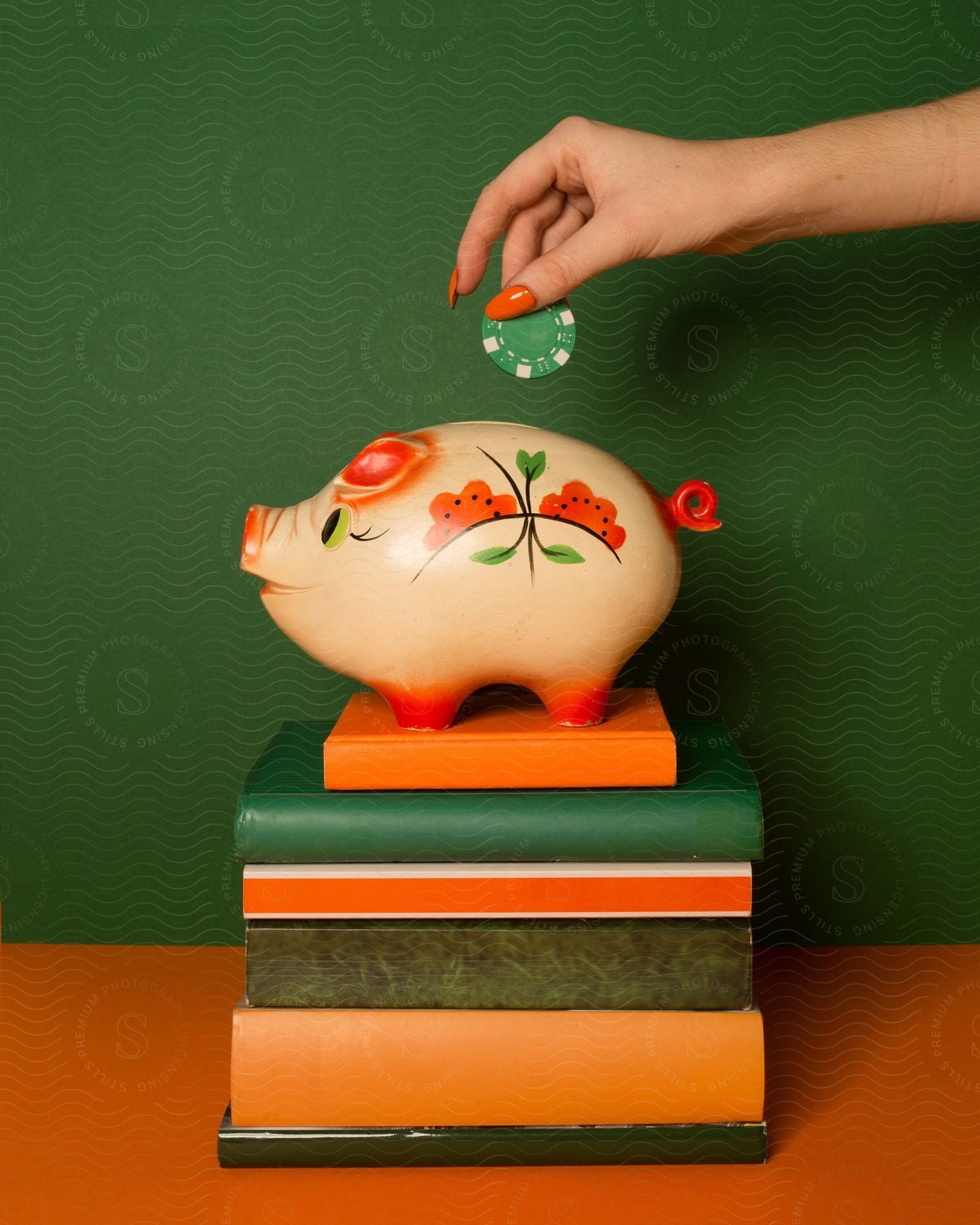 A woman's hand drops a green casino chip into a piggy bank on a stack of books, with a green background behind.