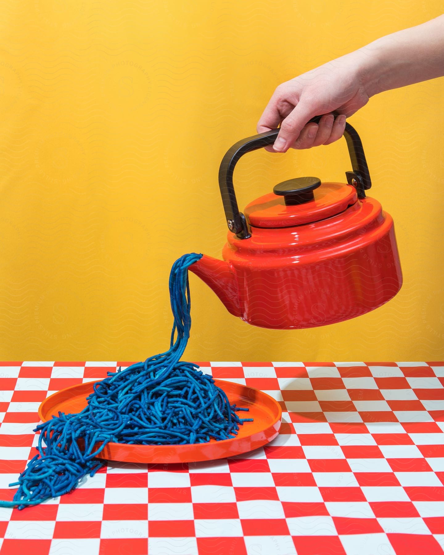 Human hand holding a vintage red kettle pouring abstract blue strands of dough.