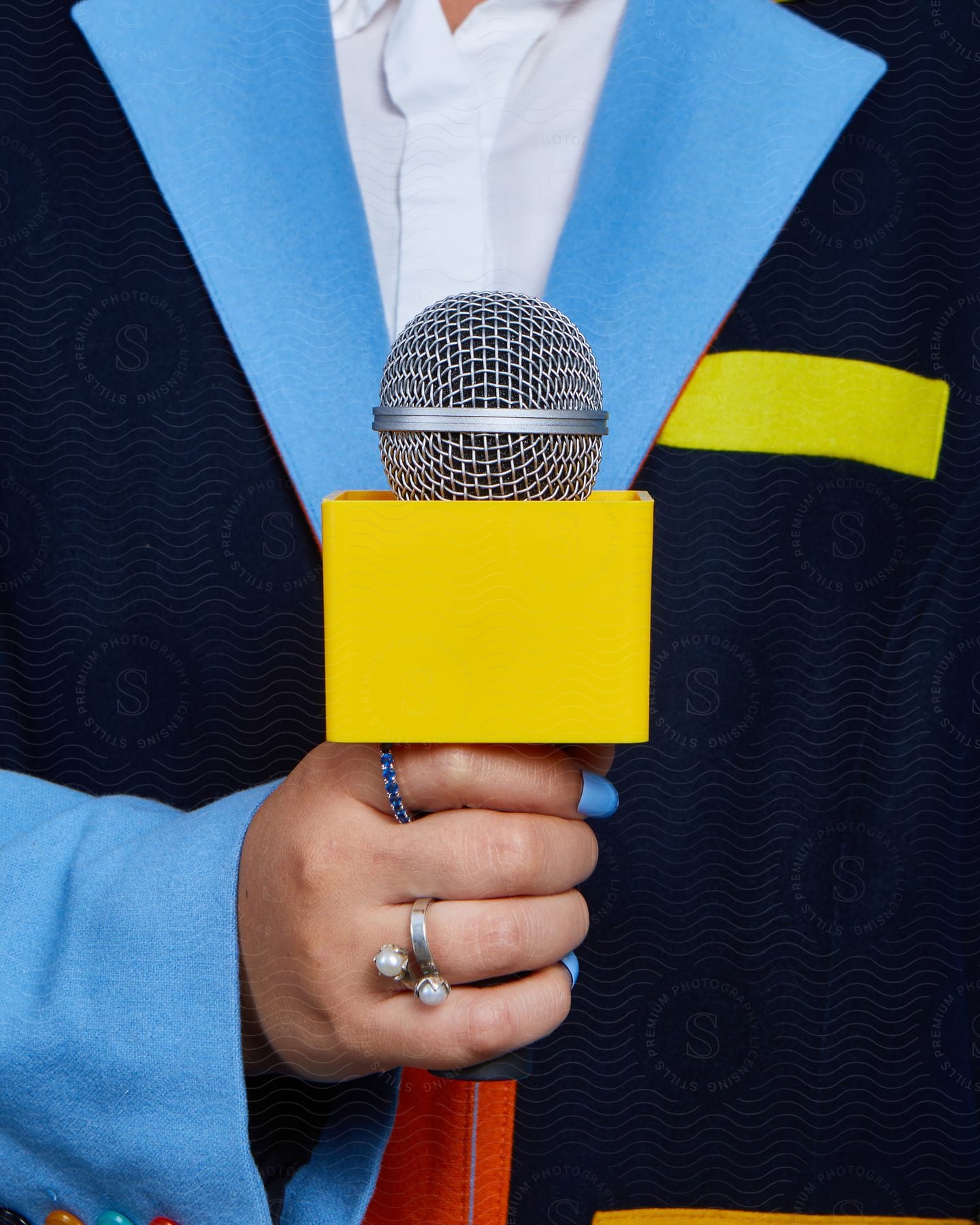 Close-up shot of a woman's hand, clad in a blue blazer jacket and white shirt, holding a yellow microphone