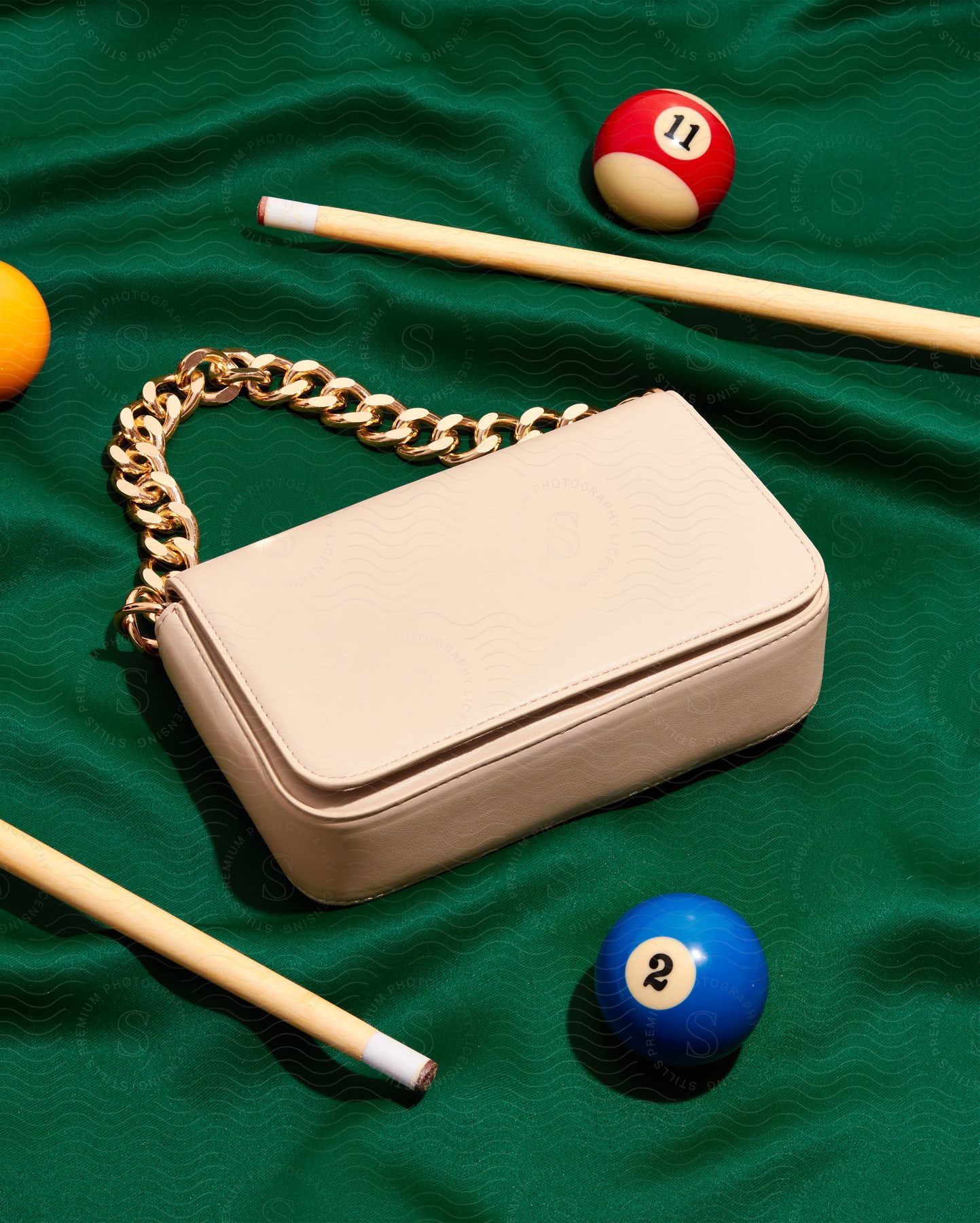 A pink purse is laying flat on a green material with pool sticks and pool balls scattered all around it.