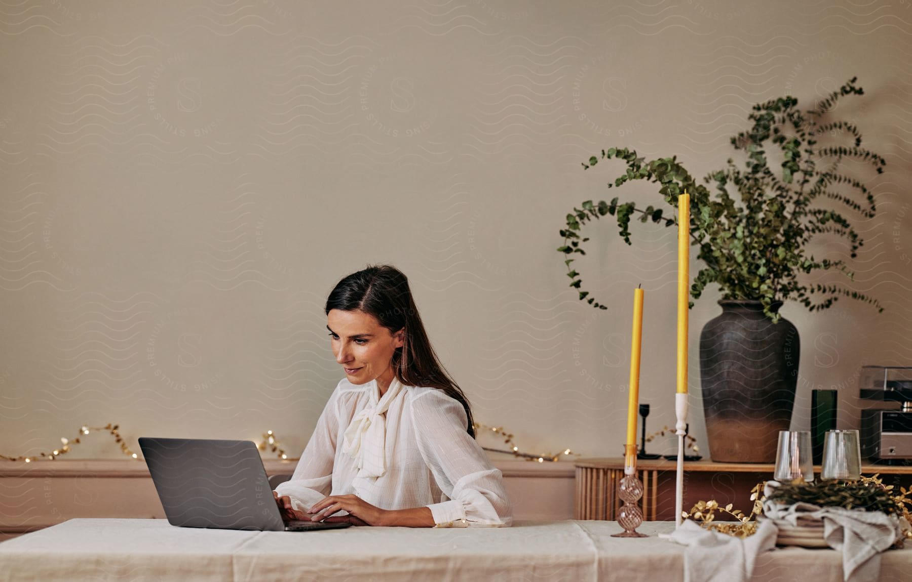 A woman is sitting at a dining room table typing on a laptop computer