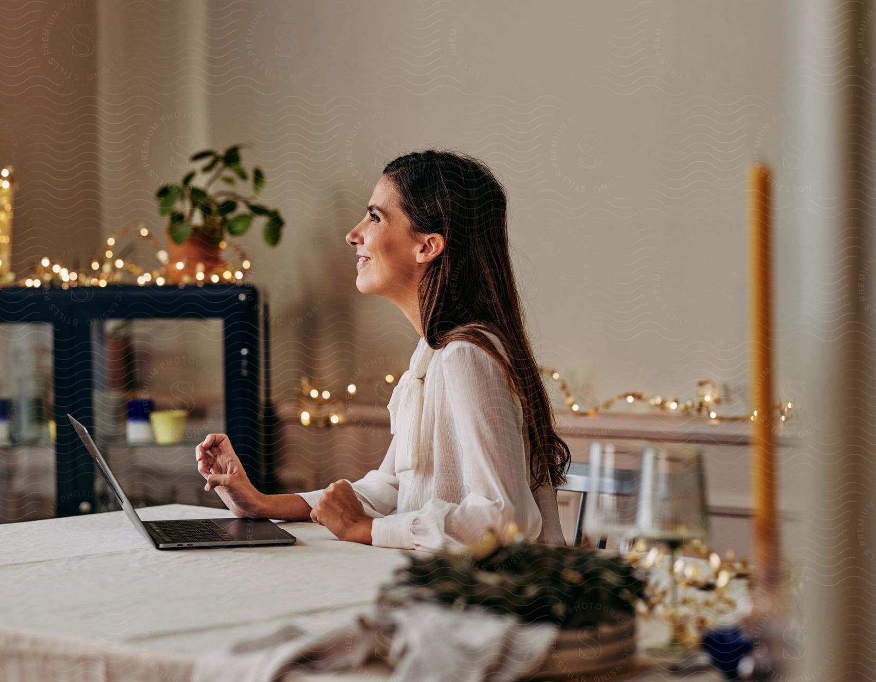 Stock photo of woman using laptop at table in brightly decorated room looks up with a smile.