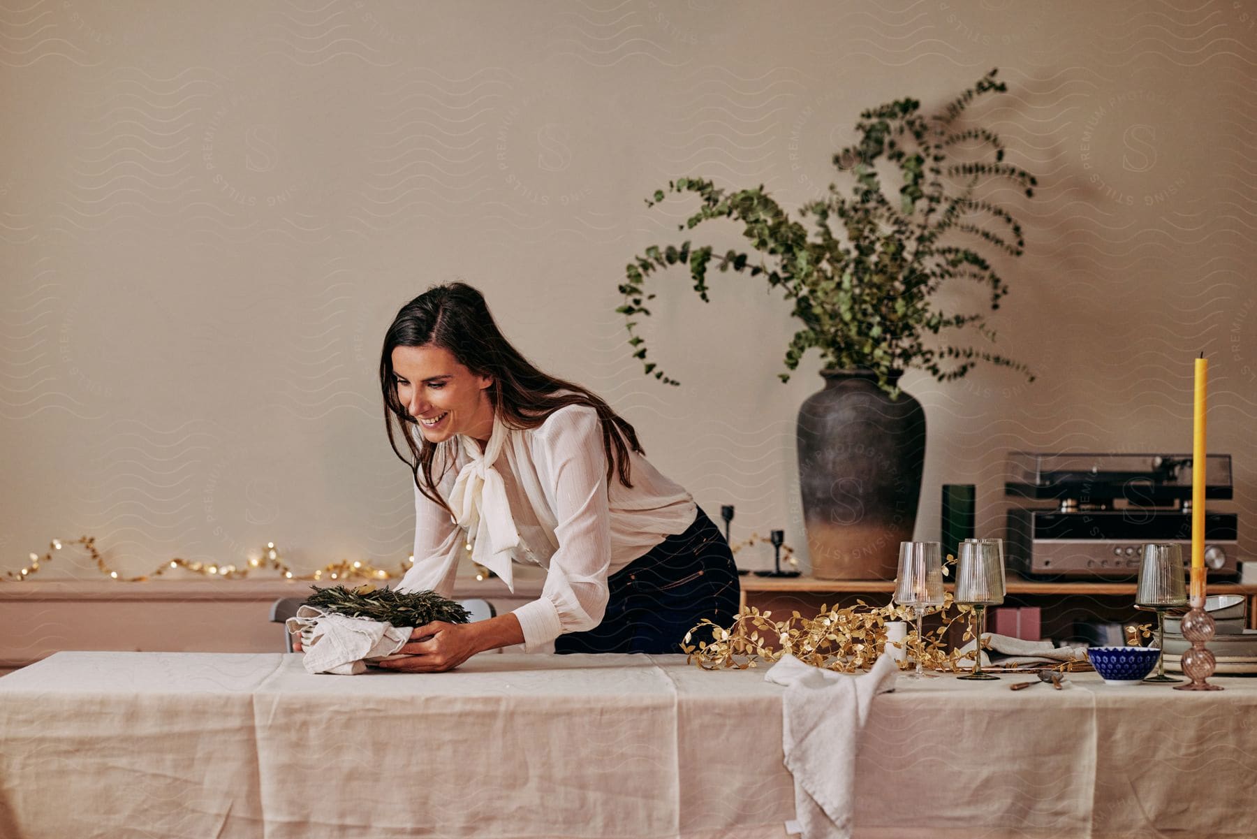 Stock photo of woman smiles while placing food onto decorated table during the holidays.