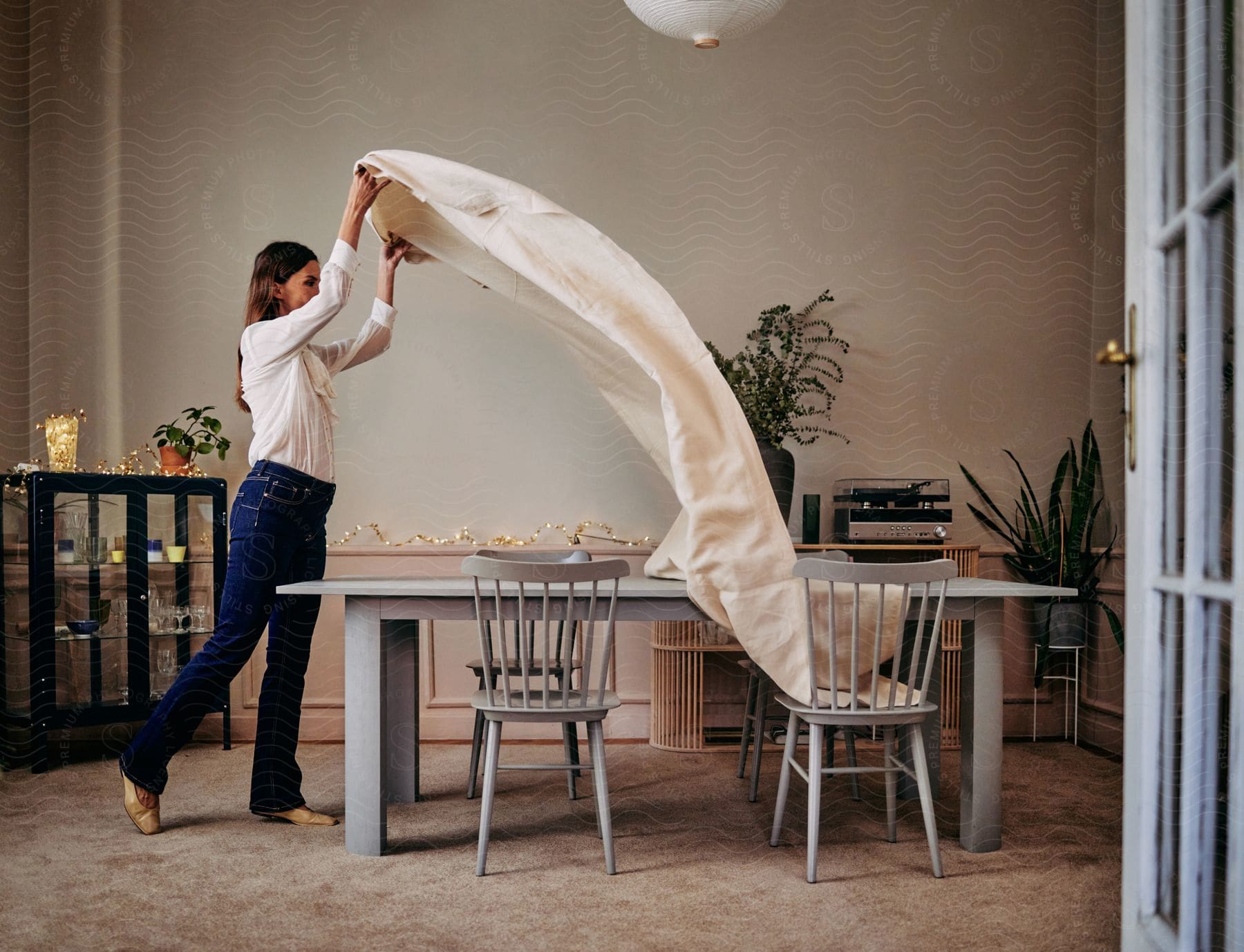 A woman stands at a dining table and drapes a table cloth over it before a meal.