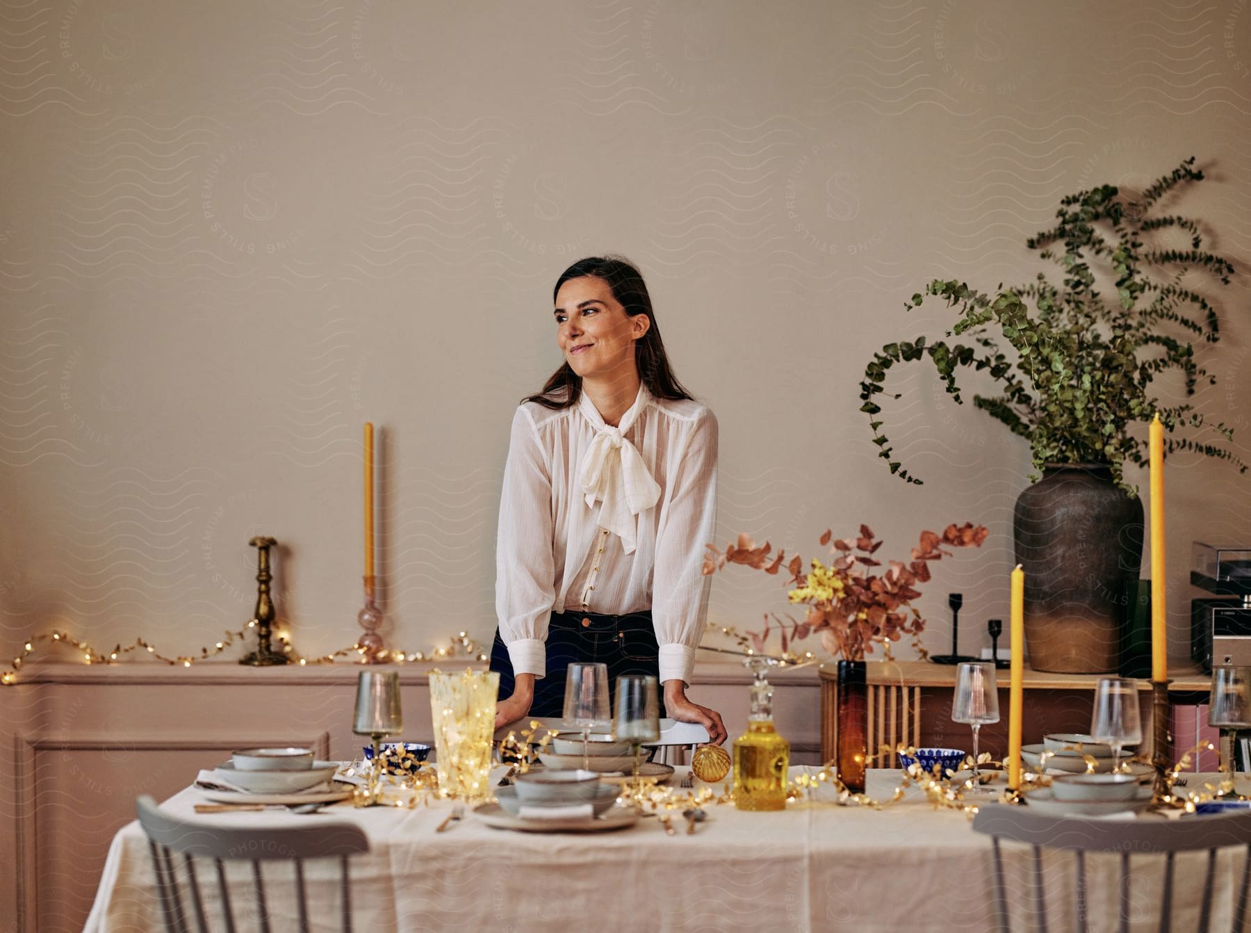 A woman in white clothes is smiling and looking to the right while setting a table with dishes.