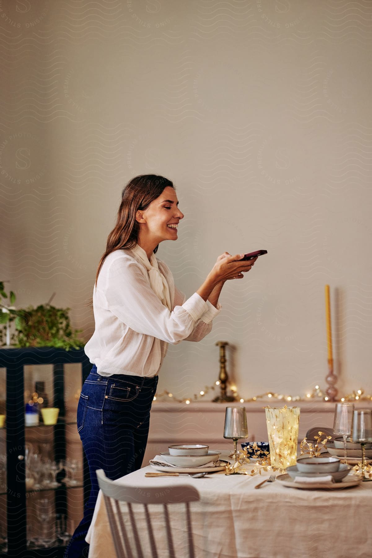 Woman with brown hair white shirt and blue jeans takes photo of table with a smartphone laughing