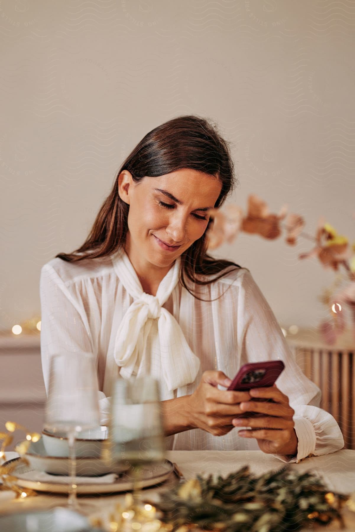 A women is sitting at the table smiling at her smartphone.