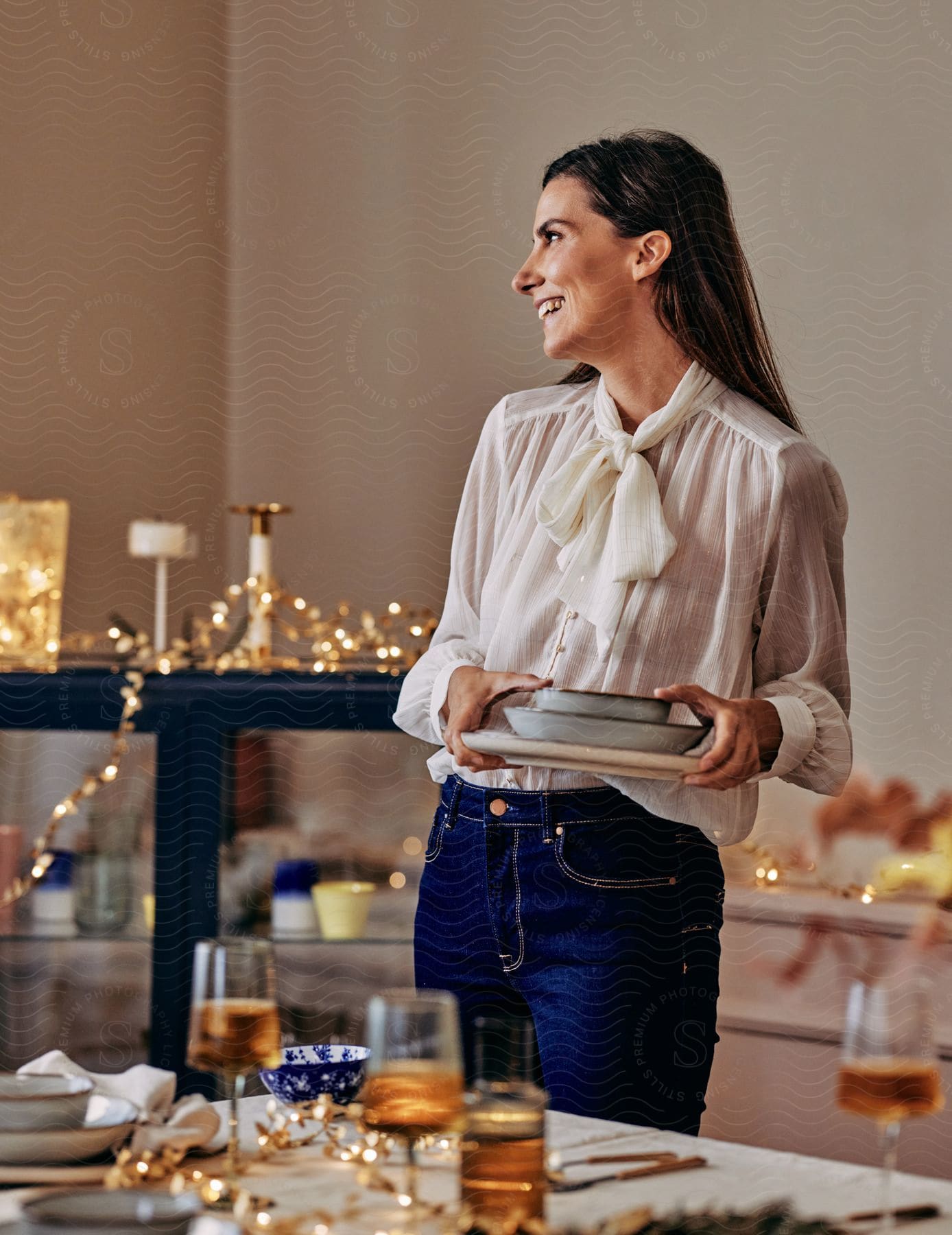 A woman holding dishes is smiling while looking to the side.