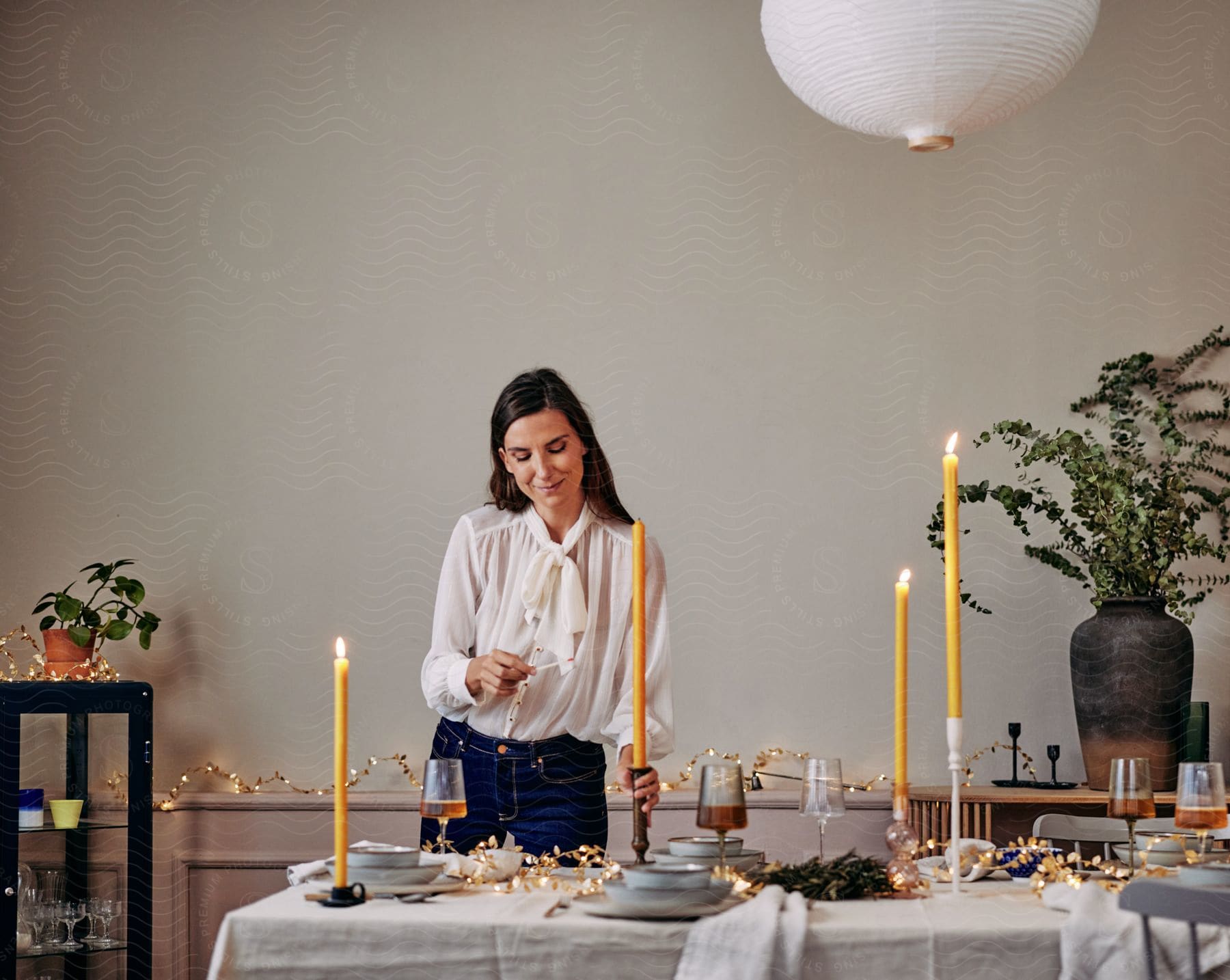 Stock photo of woman smiles while lighting tall candles for dinner party.