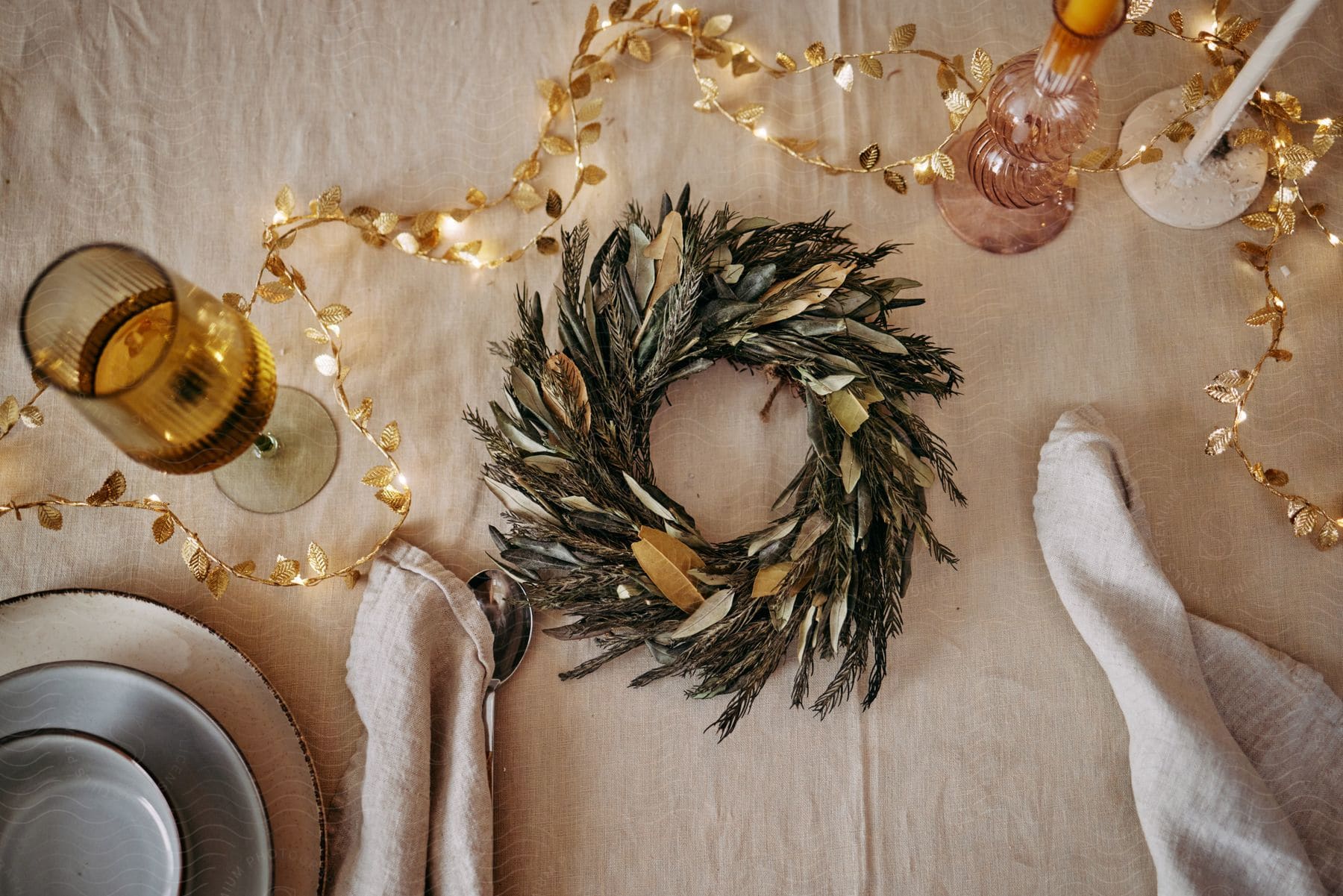 A small, green wreath sits on a dining table surrounding by tableware.