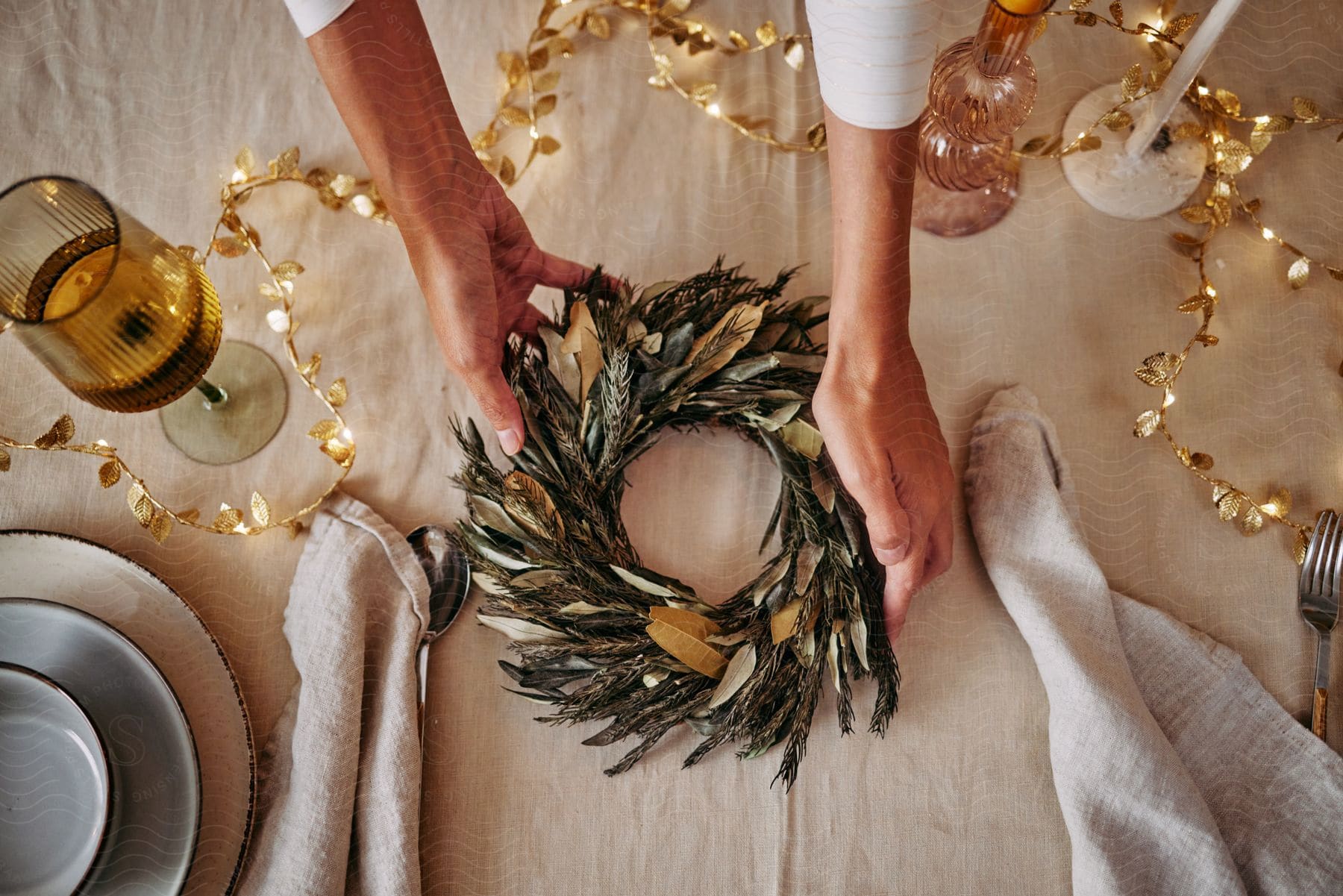 A woman positions a table wreath while setting a dining table for a meal.