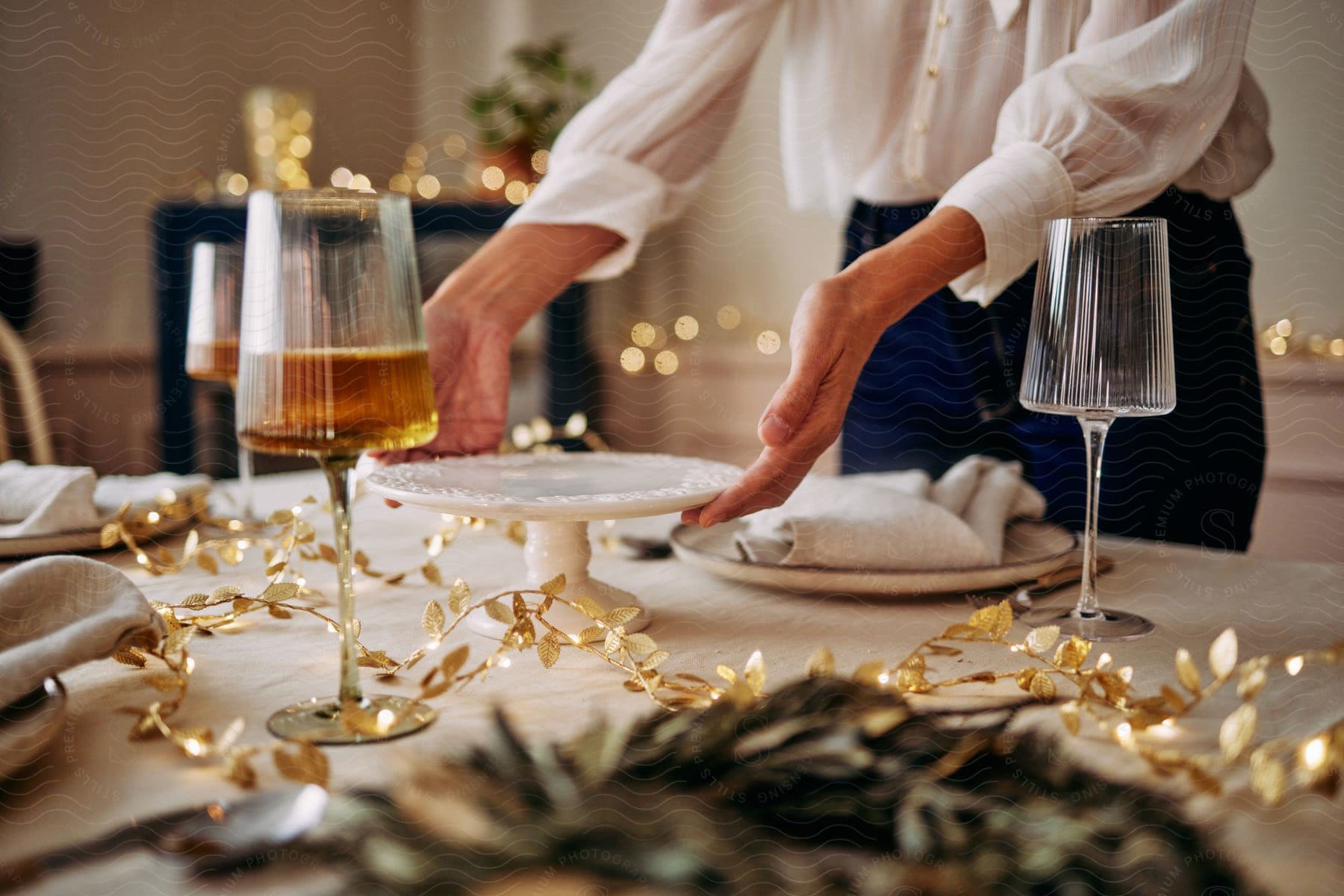 Woman in white shirt and jeans puts a cupcake stand on table near the glasses